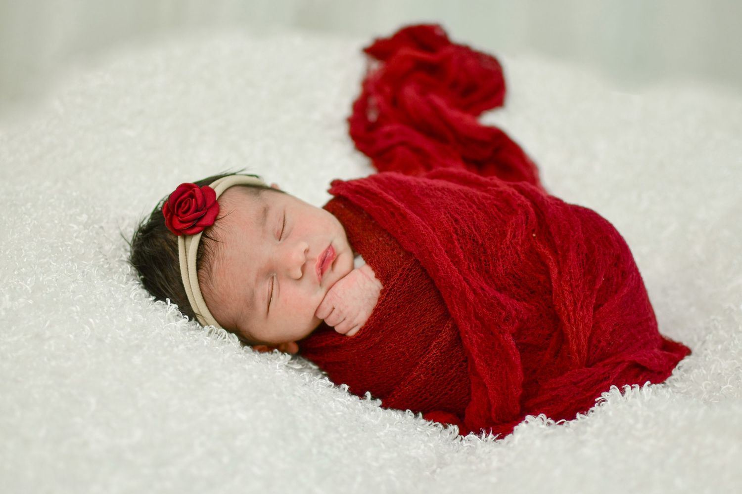 Newborn baby wrapped in red blanket sleeping on white textured surface. San Antonio newborn photography