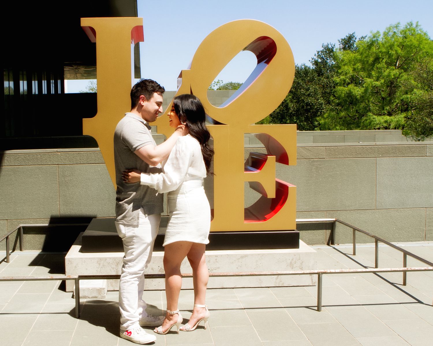 Couple embracing in front of the iconic LOVE sculpture outdoors on a sunny day.