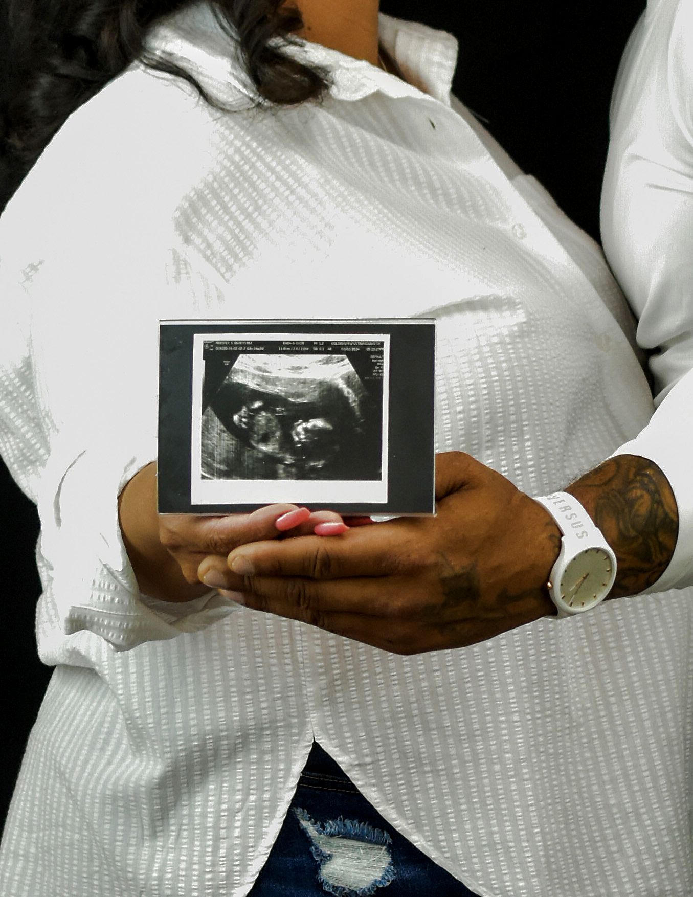 Couple in white holding ultrasound photo of baby girl while showing pregnancy announcement. Maternity photography San Antonio