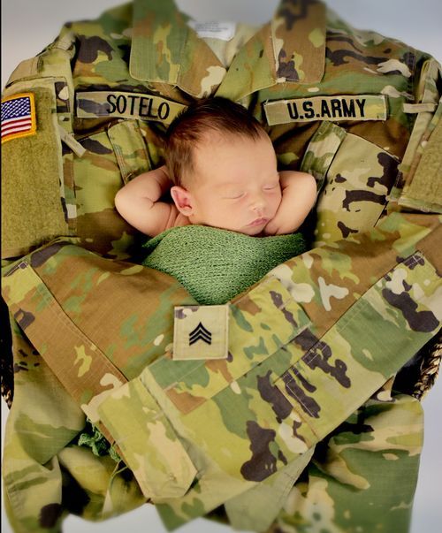 Newborn baby sleeping peacefully nestled in a U.S. Army camouflage uniform with Sotelo name tape.