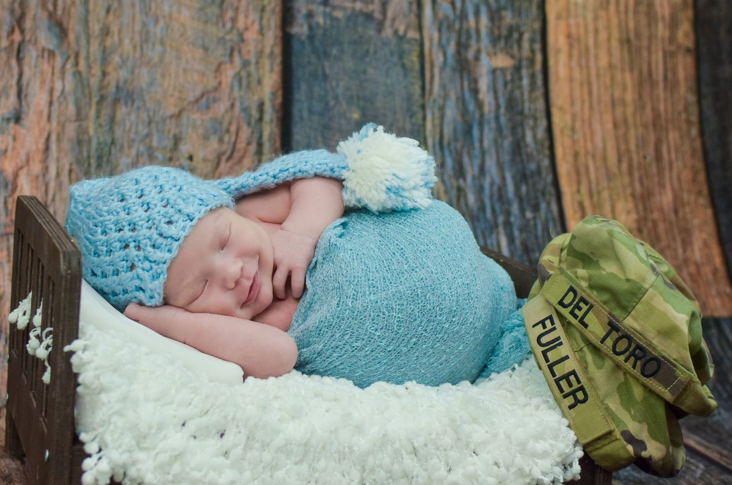 Sleeping newborn baby wearing a blue knit hat and wrapped in a soft blue blanket in a rustic wooden box.