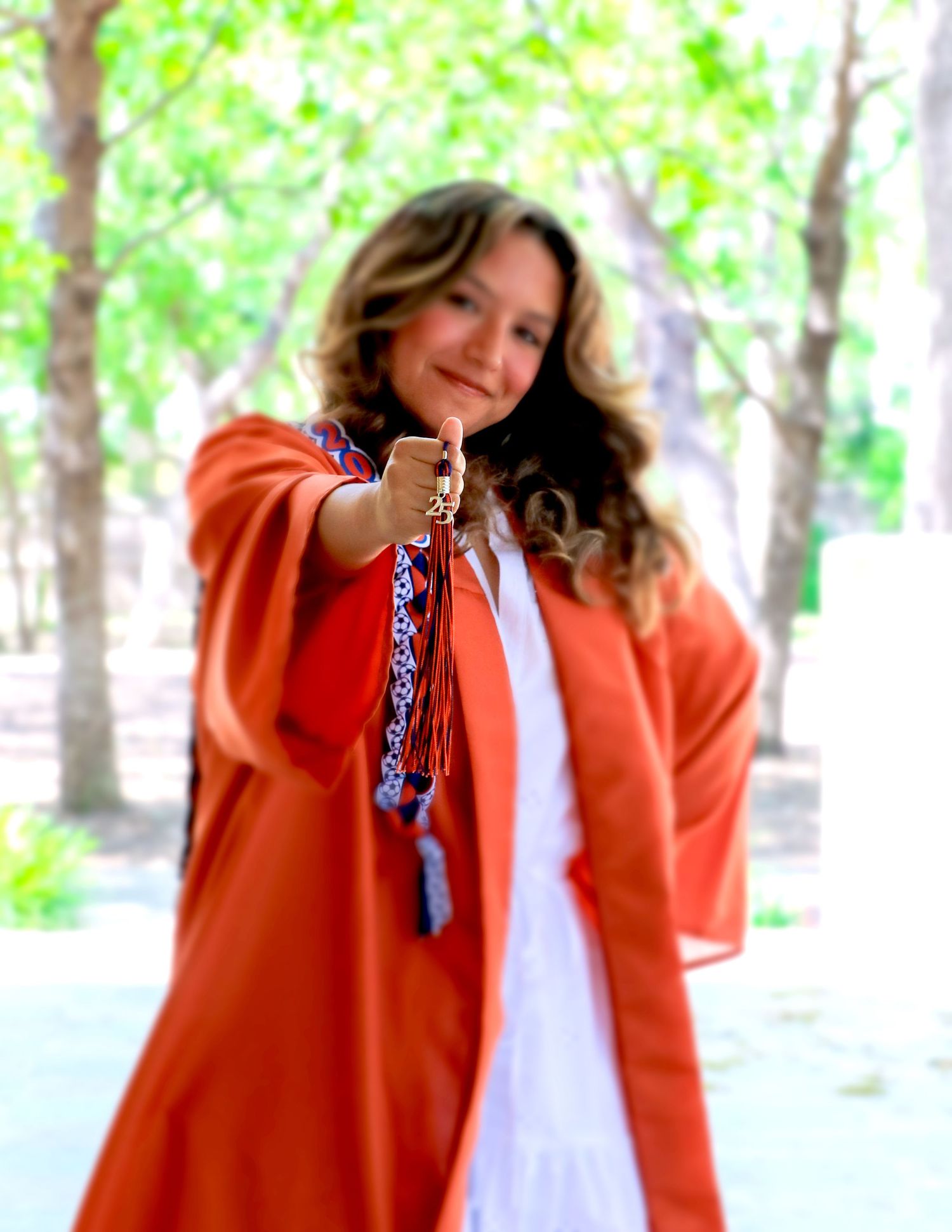 A graduate in a bright orange gown and white dress poses playfully at her senior photography session at Landa Library in San Antonio.