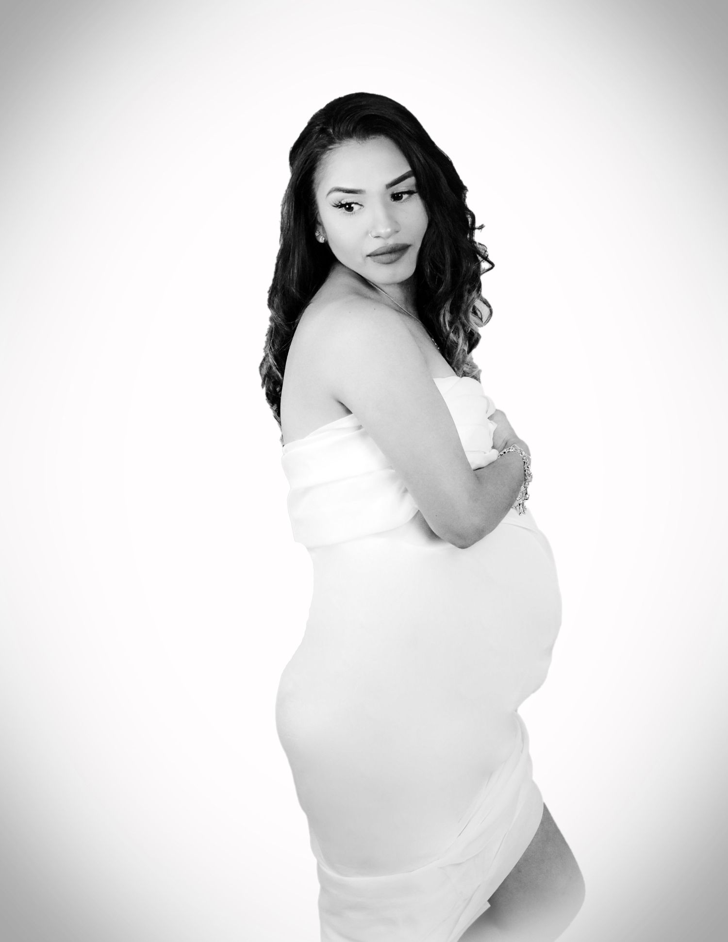 Artistic black and white maternity portrait showing an elegant pose against a white background with dramatic lighting in San Antonio, Texas