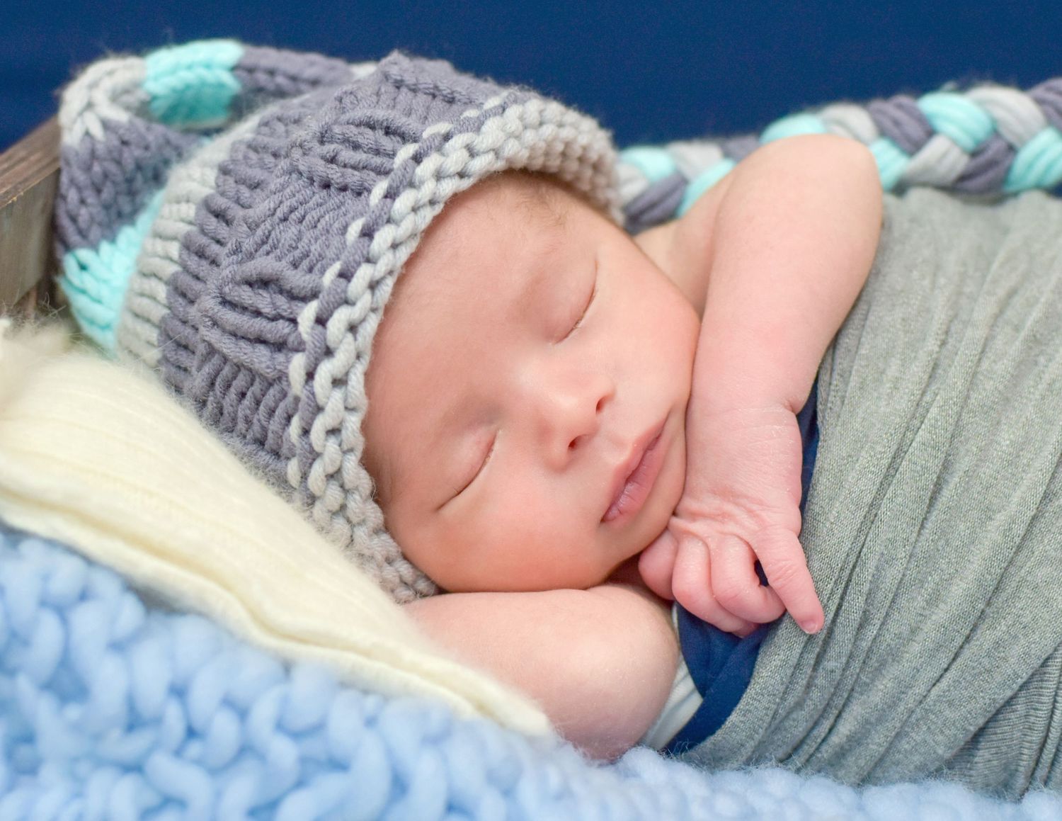 Peaceful newborn baby sleeping in a gray knit hat, swaddled in soft blue and gray blankets.