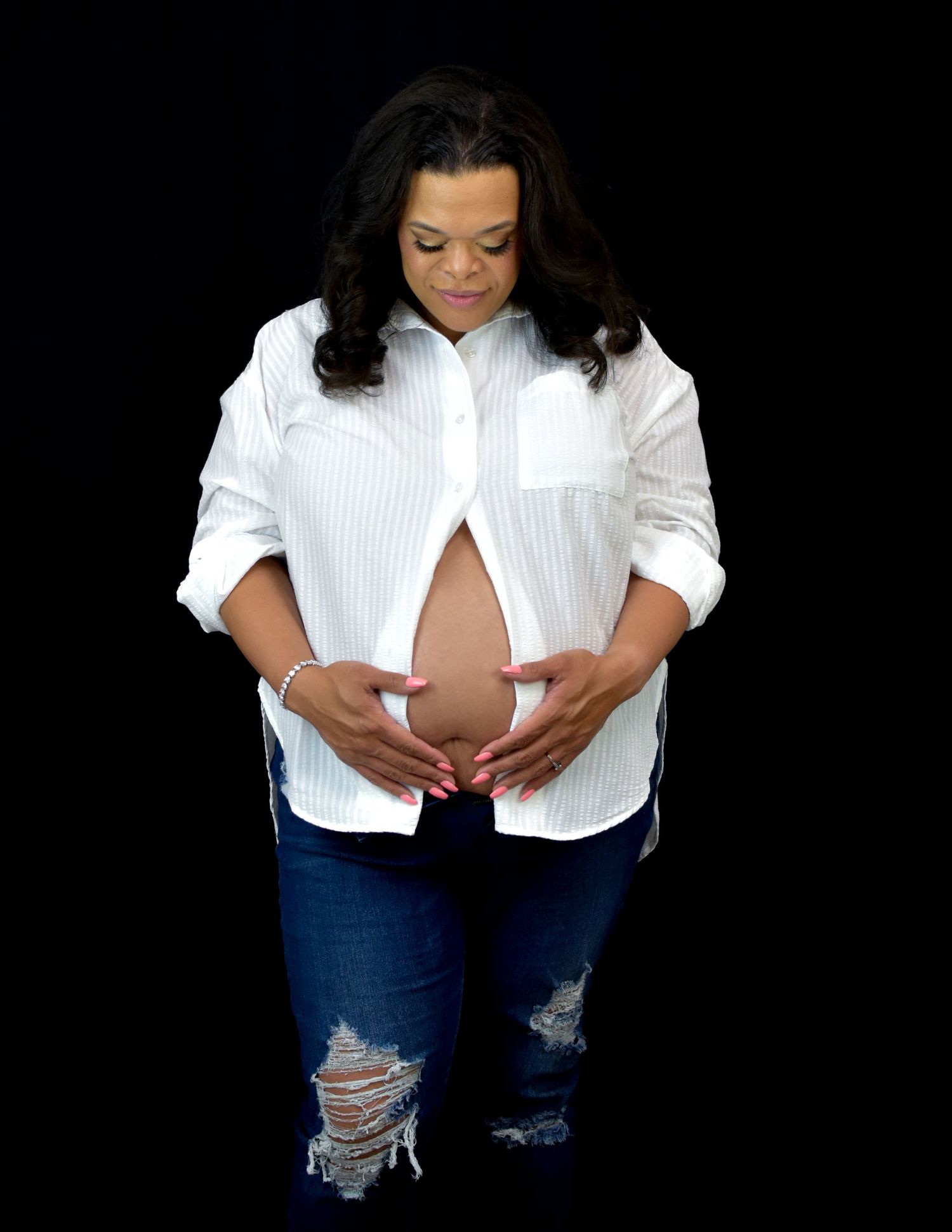 Mom to be wearing a white button-down shirt and distressed jeans poses in a series of maternity style photos in San Antonio, Texas