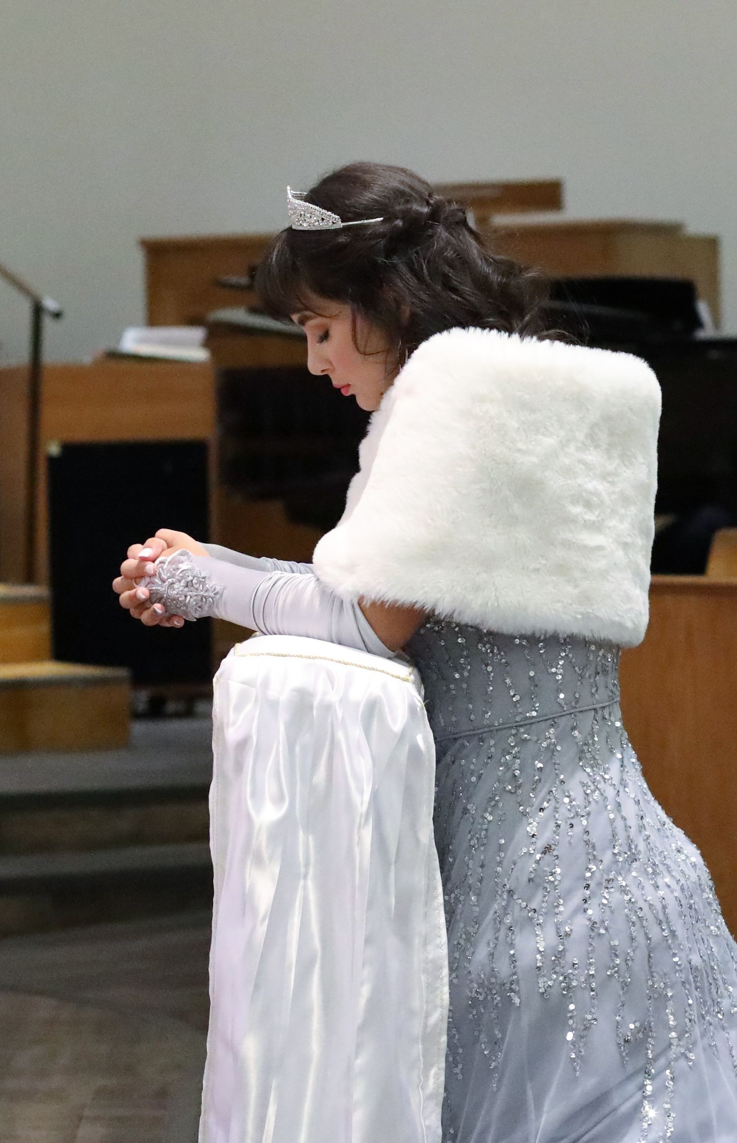 Quinceanera wearing a beaded silver gown, white fur stole, and tiara during her special event. San Antonio photographer.