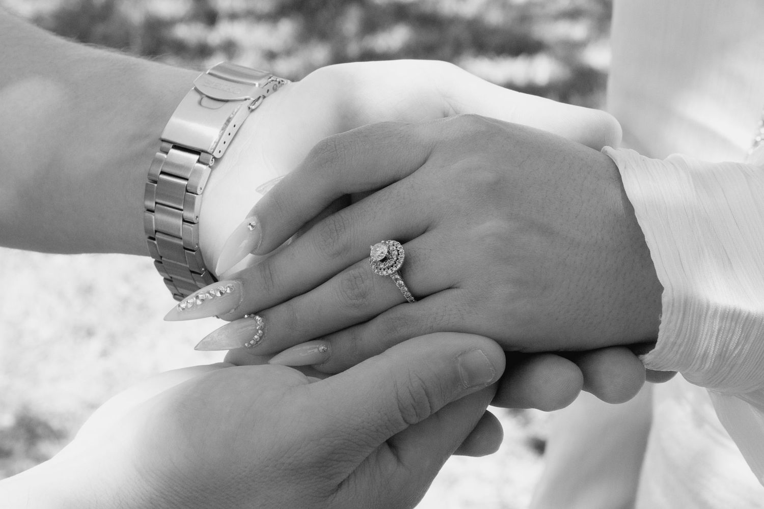 Black and white photo of couple holding hands, woman wearing diamond engagement ring and man wearing watch.