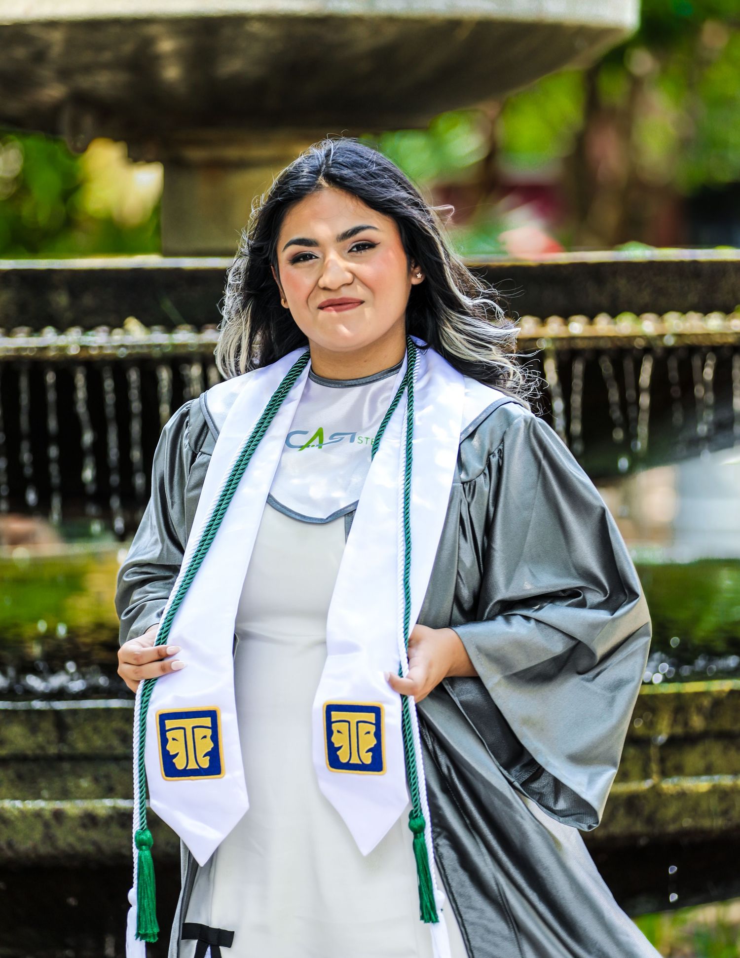 Graduate with white stole and silver gown poses outdoors at The Pearl in San Antonio during her senior graduation photo session.