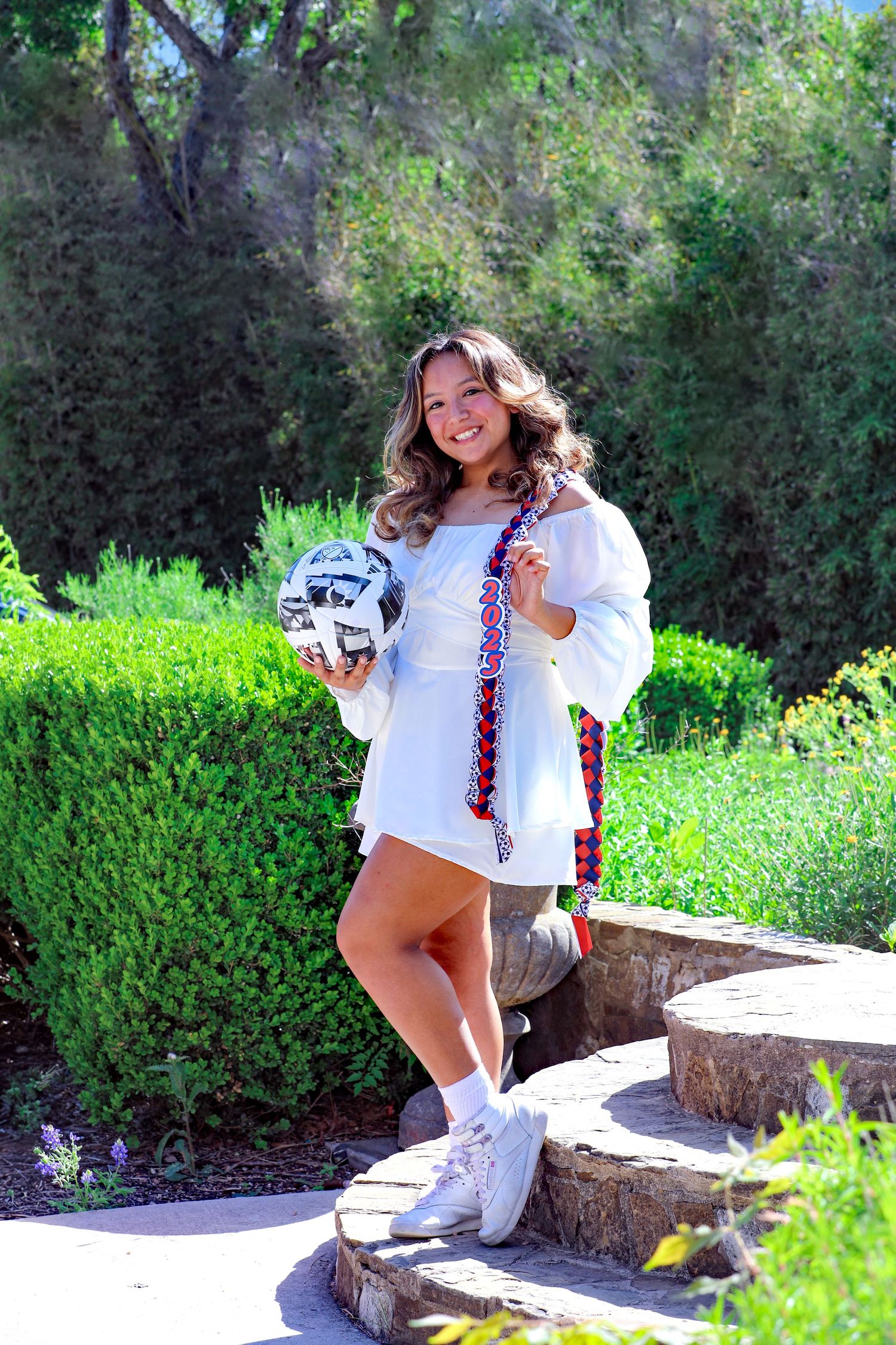A Madison HS graduate wearing white dress and boots posing at Landa Library in San Antonio, Texas at her senior photography session.