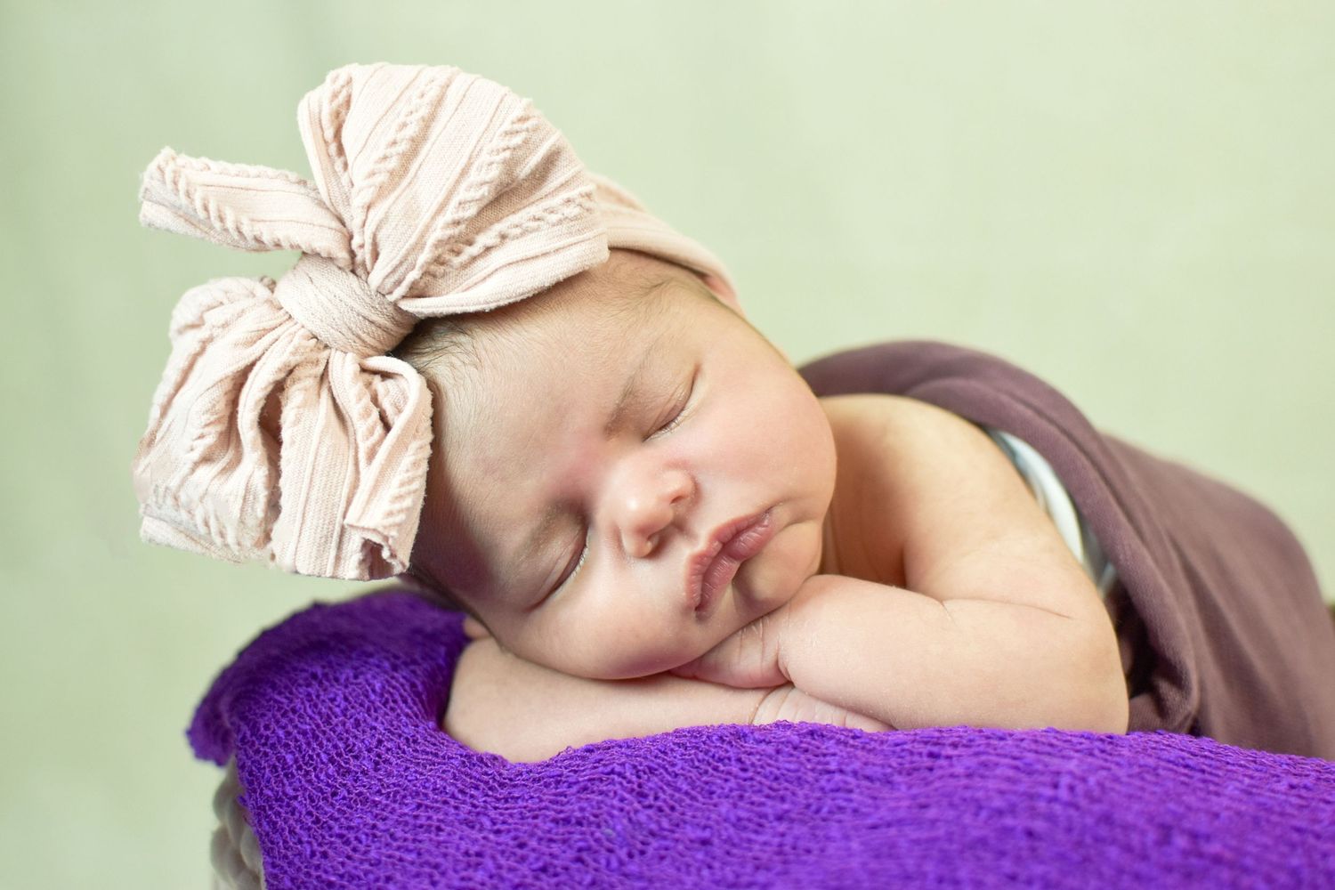 Peaceful newborn sleeping on purple cushion with striped bow headband. San Antonio newborn photography