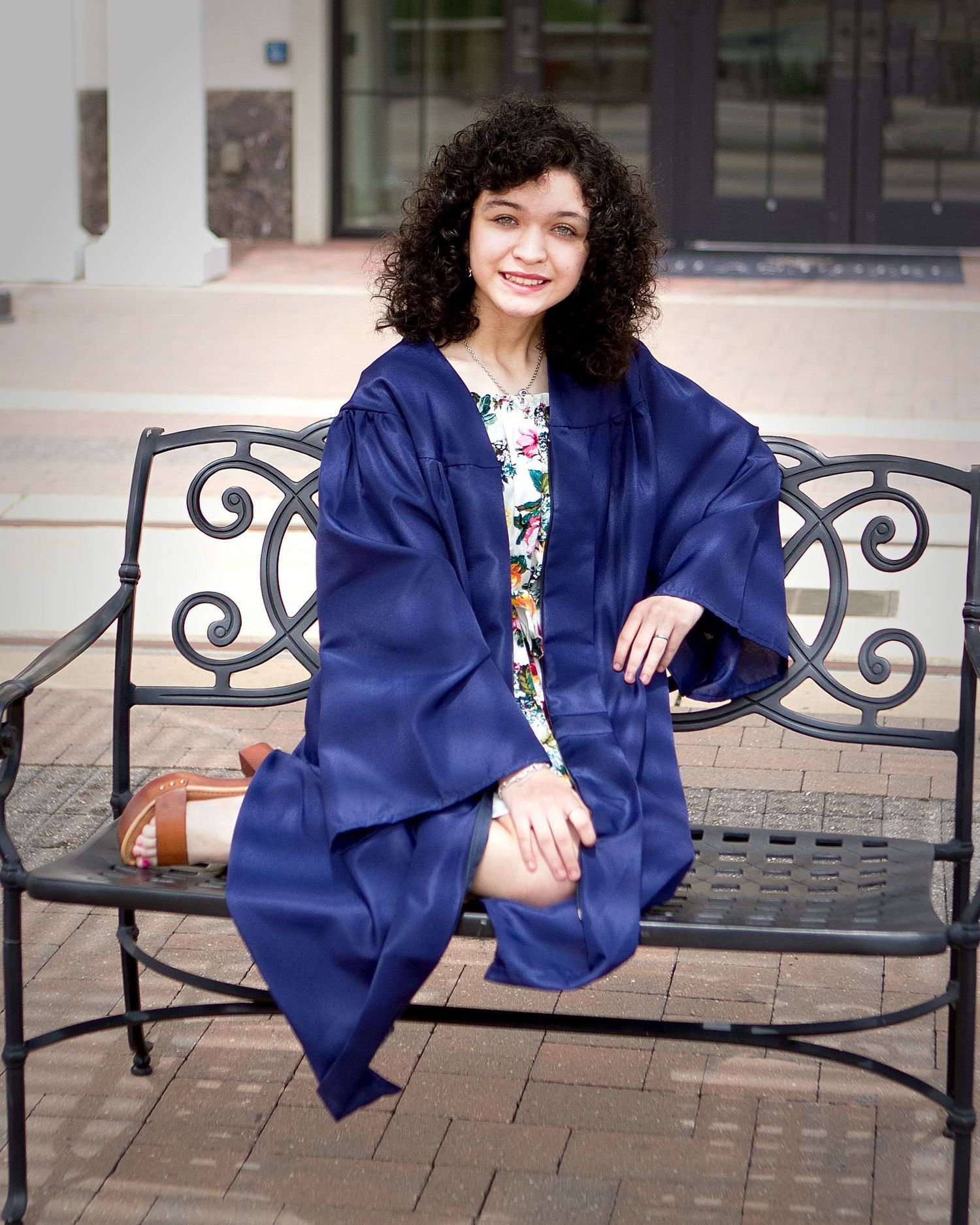 A graduate in a navy gown poses on a decorative bench at the Eilan Hotel & Spa grounds during a graduation photoshoot in San Antonio.