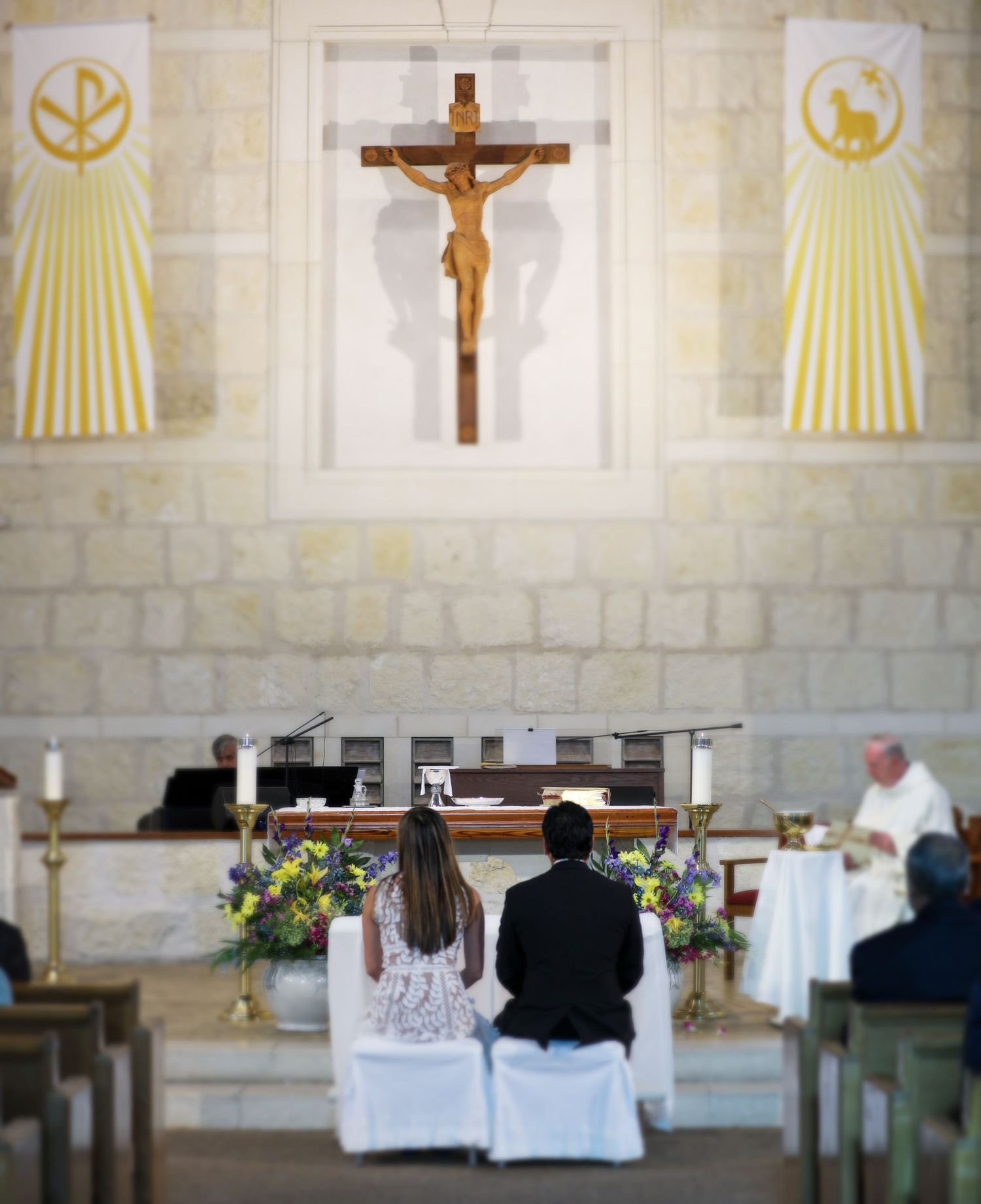 Couple kneeling at church altar during wedding ceremony with crucifix and religious banners in background.