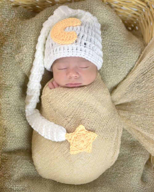Newborn baby swaddled in cream wrap wearing a crochet nightcap with moon, sleeping peacefully in a basket.