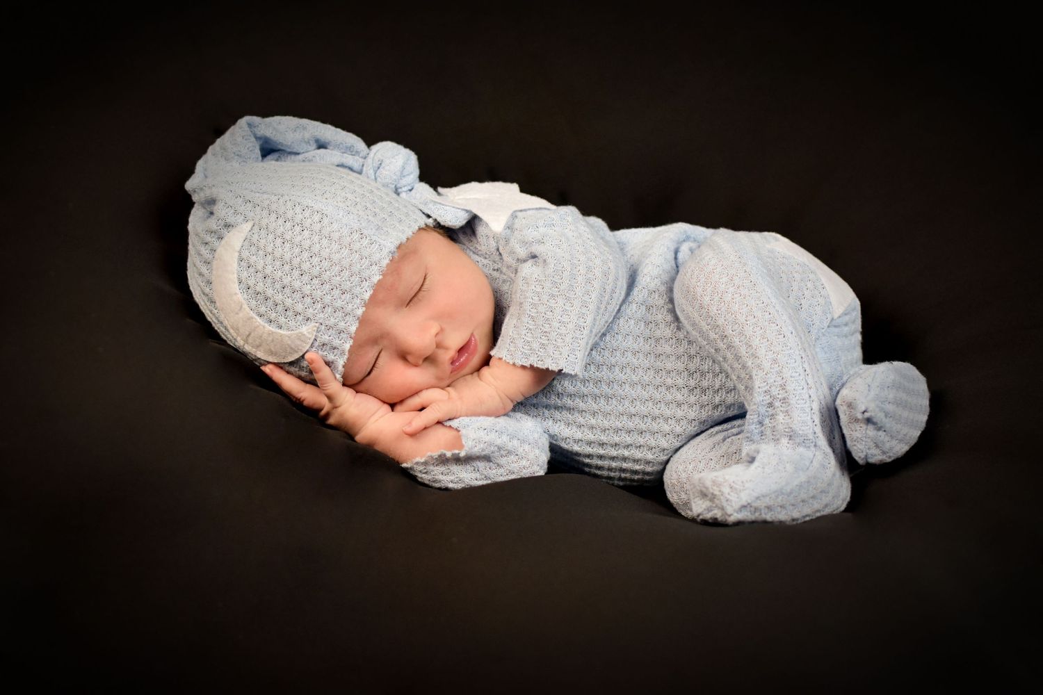 Sleeping baby in light blue outfit against dark background. San Antonio newborn photography