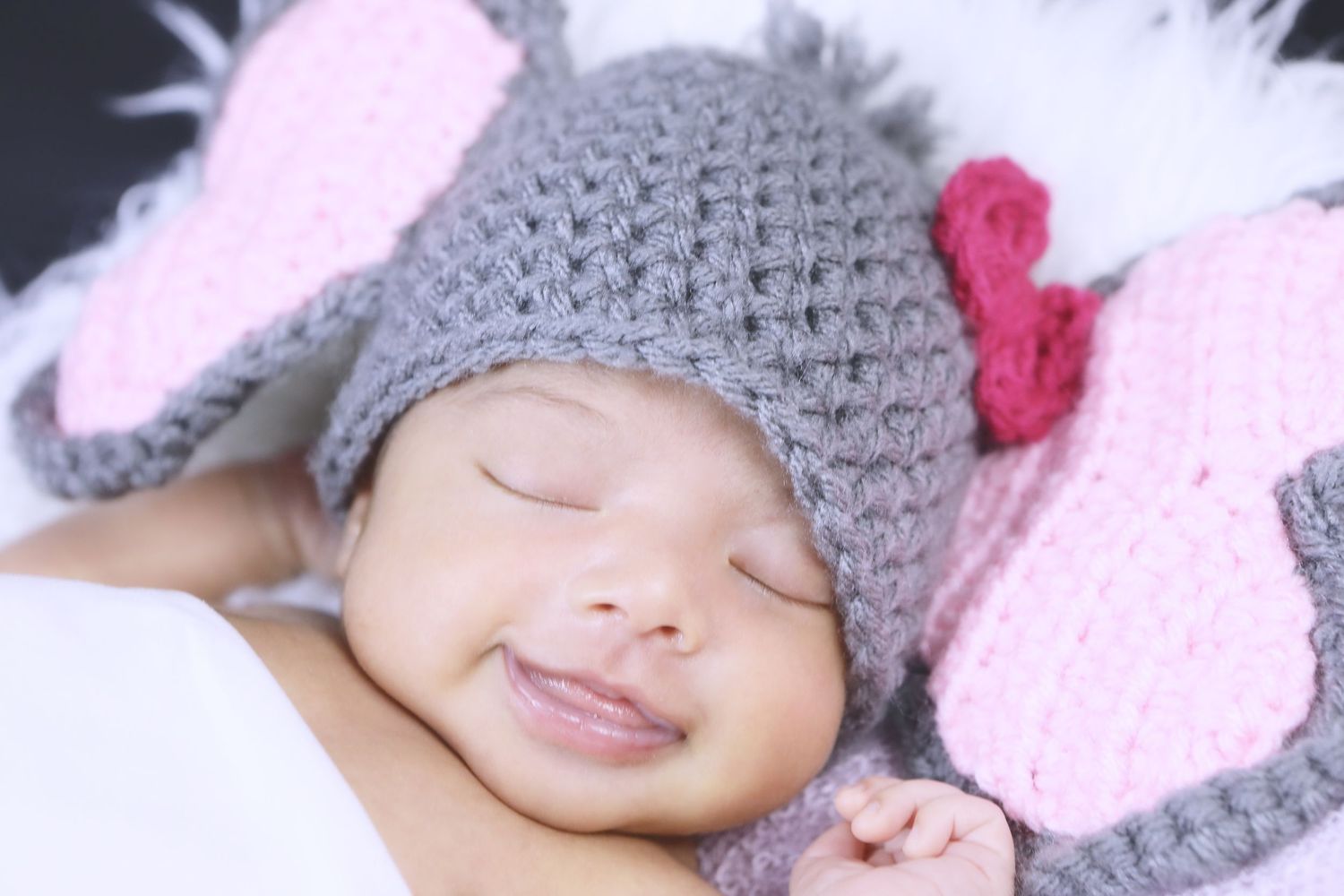 Sleeping newborn wearing grey knit elephant hat with pink flower on pink background. San Antonio newborn photography