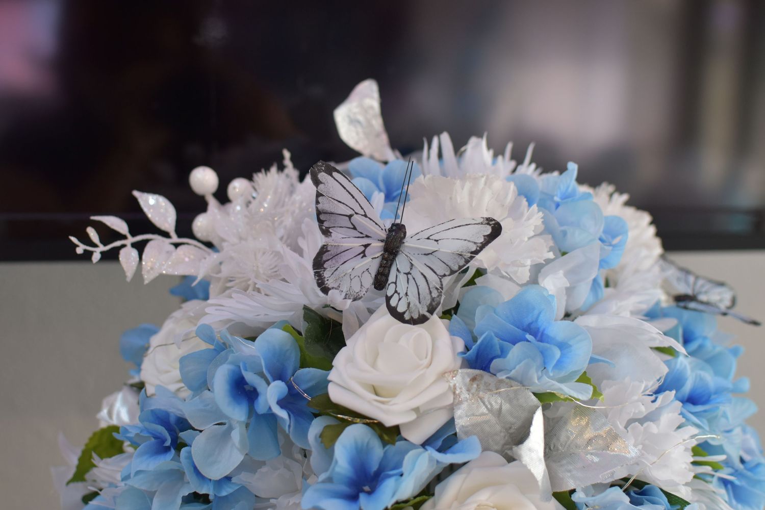 Elegant floral arrangement featuring blue hydrangeas, white roses and delicate butterfly accents in a decorative setting at a Sweet 16 event