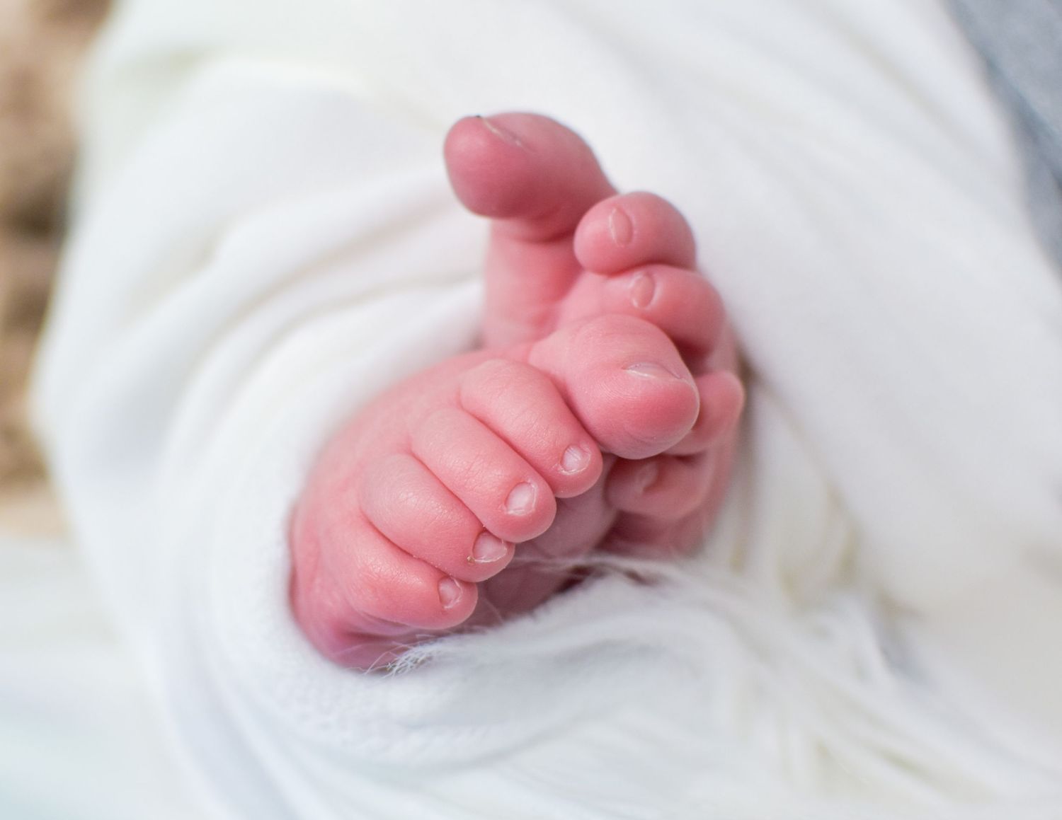Close-up of tiny newborn baby toes wrapped in a soft white blanket, showcasing delicate pink skin and small nails.