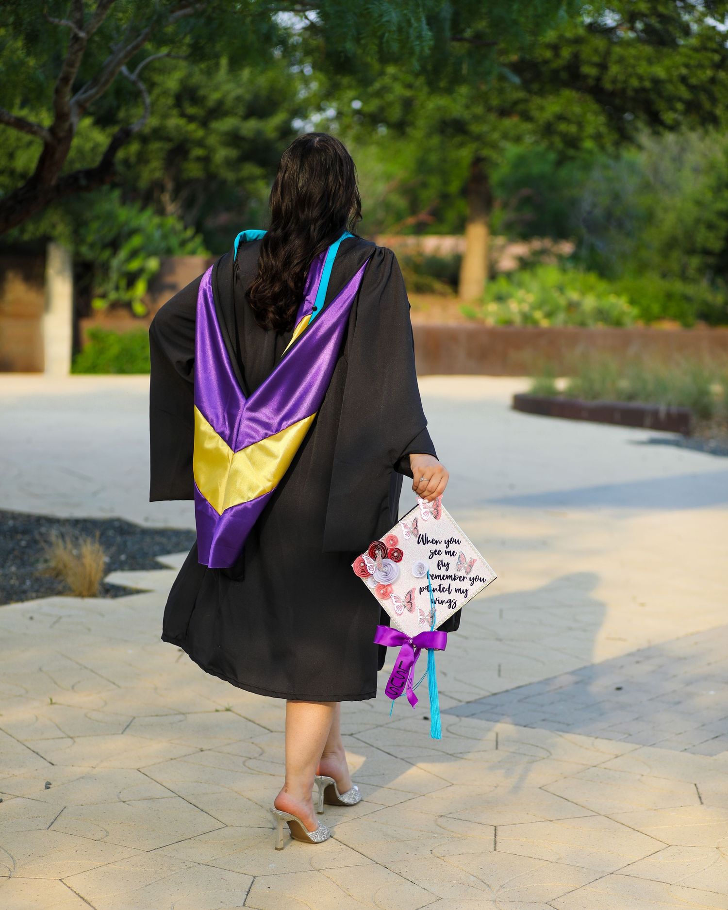 Graduate in black graduation gown walking with purple stole and holding cap during graduation senior photography session in San Antonio.