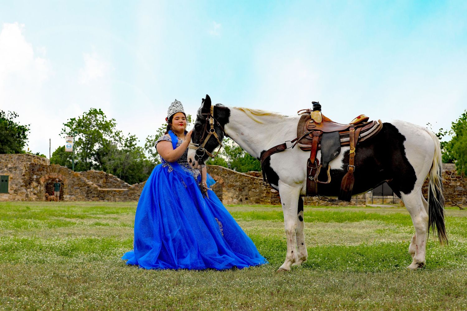 Amazing quinceanera in blue gown and crown poses with a white horse outdoors at the Missions in San Antonio. Precious Keepsakes Photography