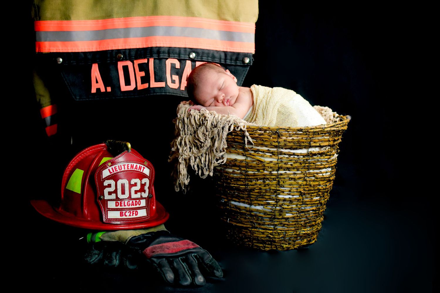 Red firefighter helmet and jacket arranged in a dark rustic setting with baby nestled in bucket with white, San Antonio newborn photography