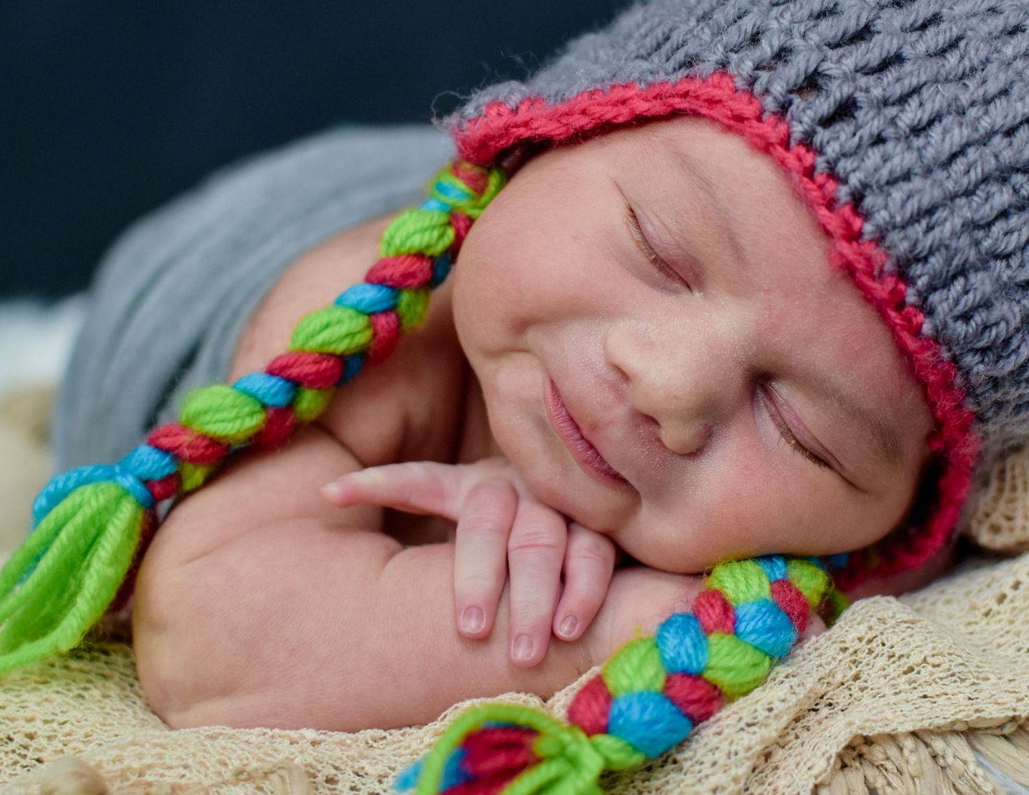 Smiling newborn baby boy sleeping peacefully wearing a colorful knit hat photographed by Precious Keepsakes Photography San Antonio & Boerne