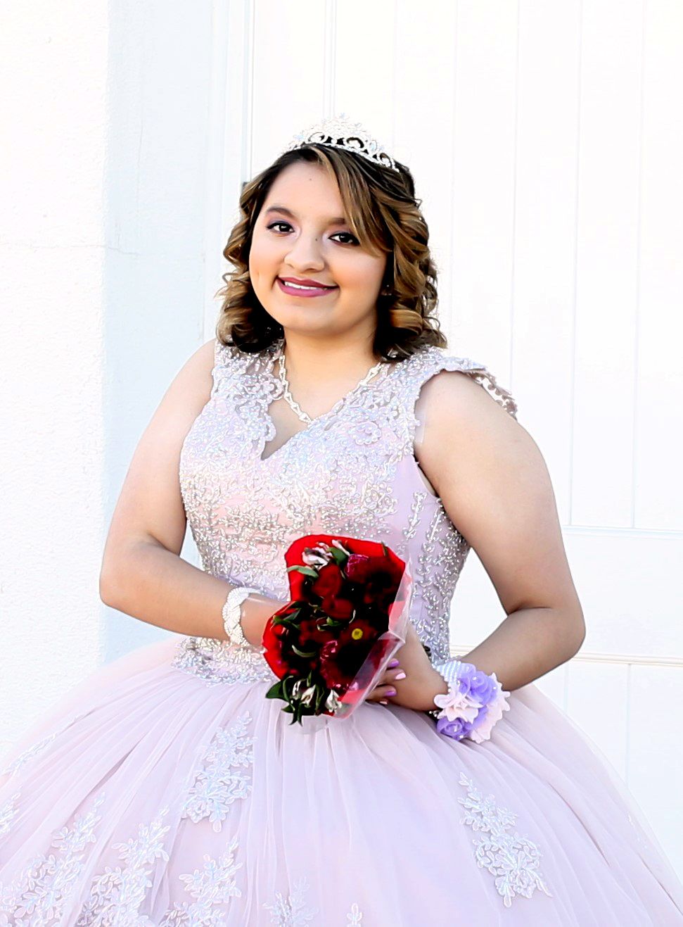 A quinceanera in her light pink dress with lace details poses with a red rose bouquet at St Anthony de Padua in San Antonio photo session.