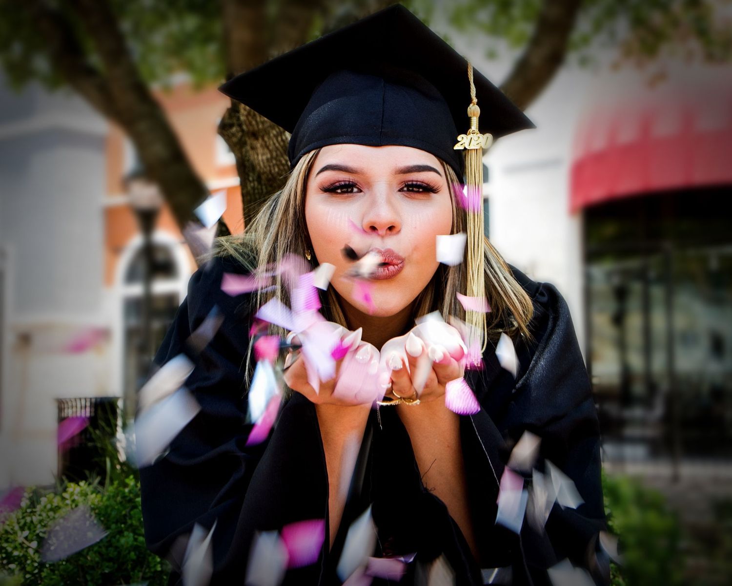 A graduate in cap and gown blowing pink confetti towards the camera in celebration. San Antonio senior photographer