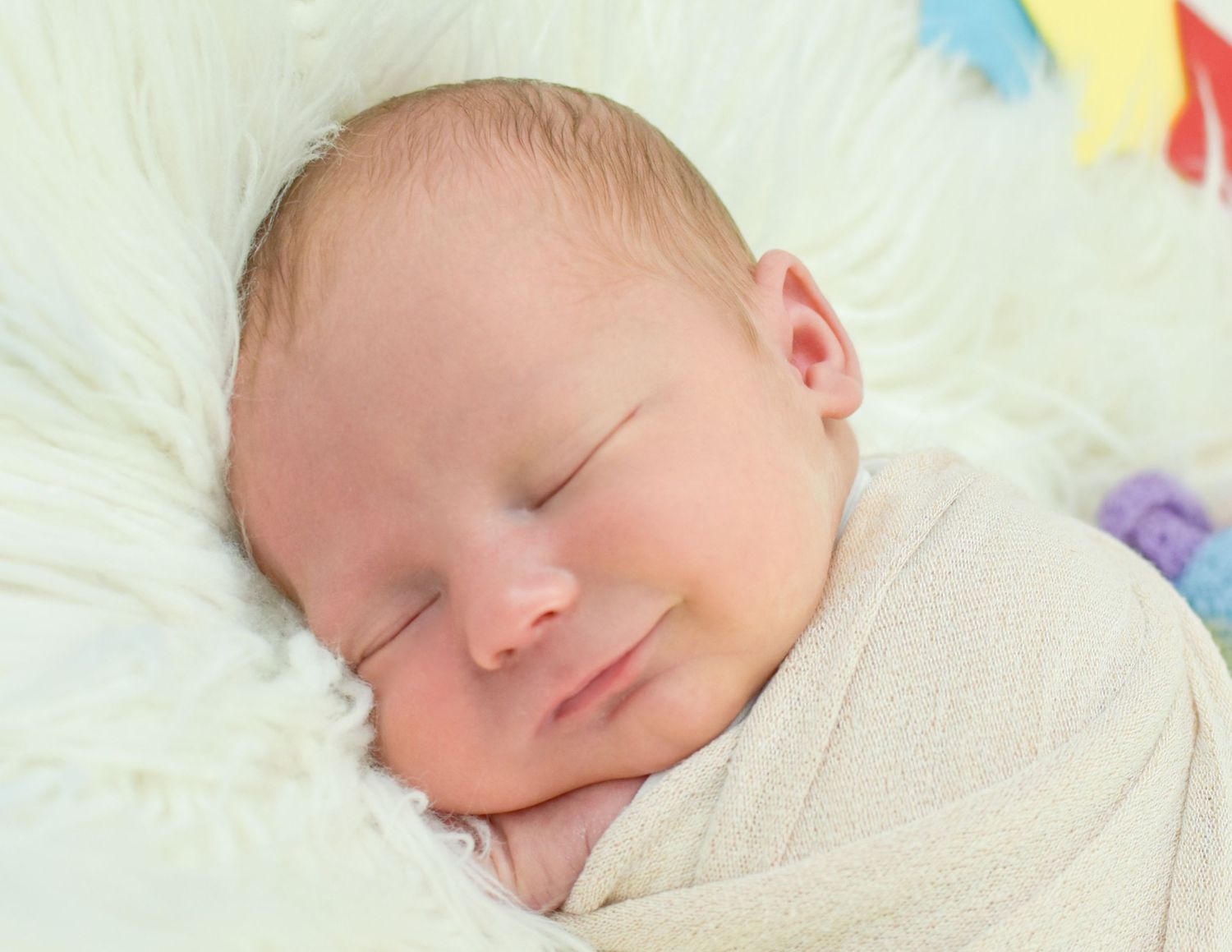 Peaceful newborn baby sleeping swaddled in white blanket with soft smile on fluffy white background.