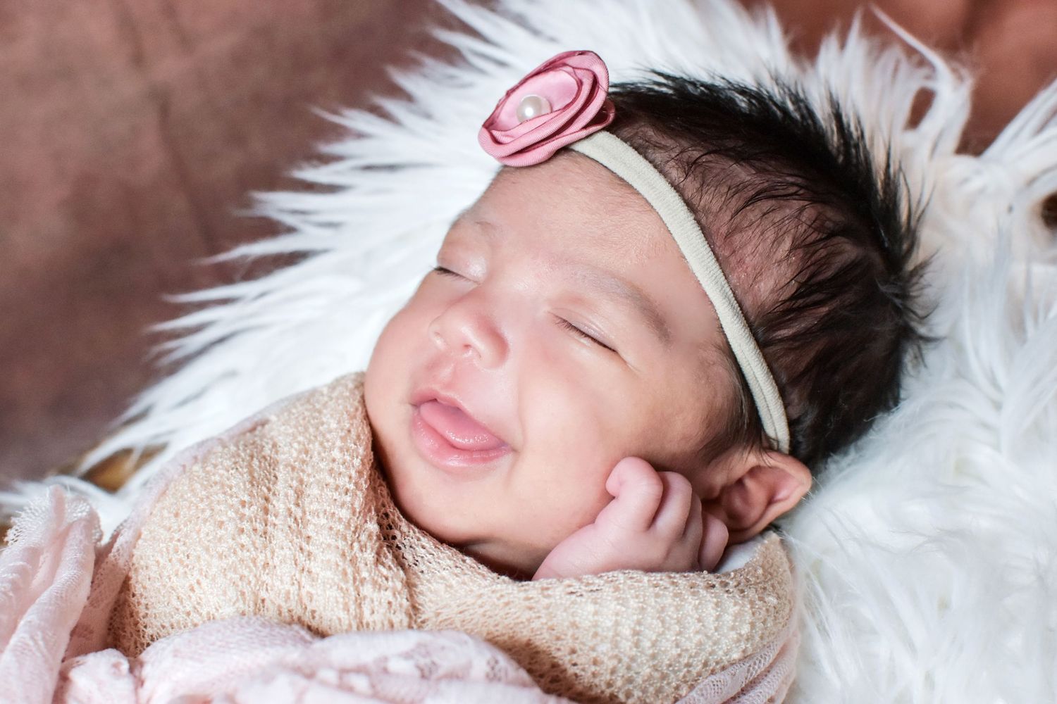 Newborn photography. Smiling newborn baby girl swaddled in a soft blanket on a fluffy white fur surface. Precious keepsakes San Antonio. Tx