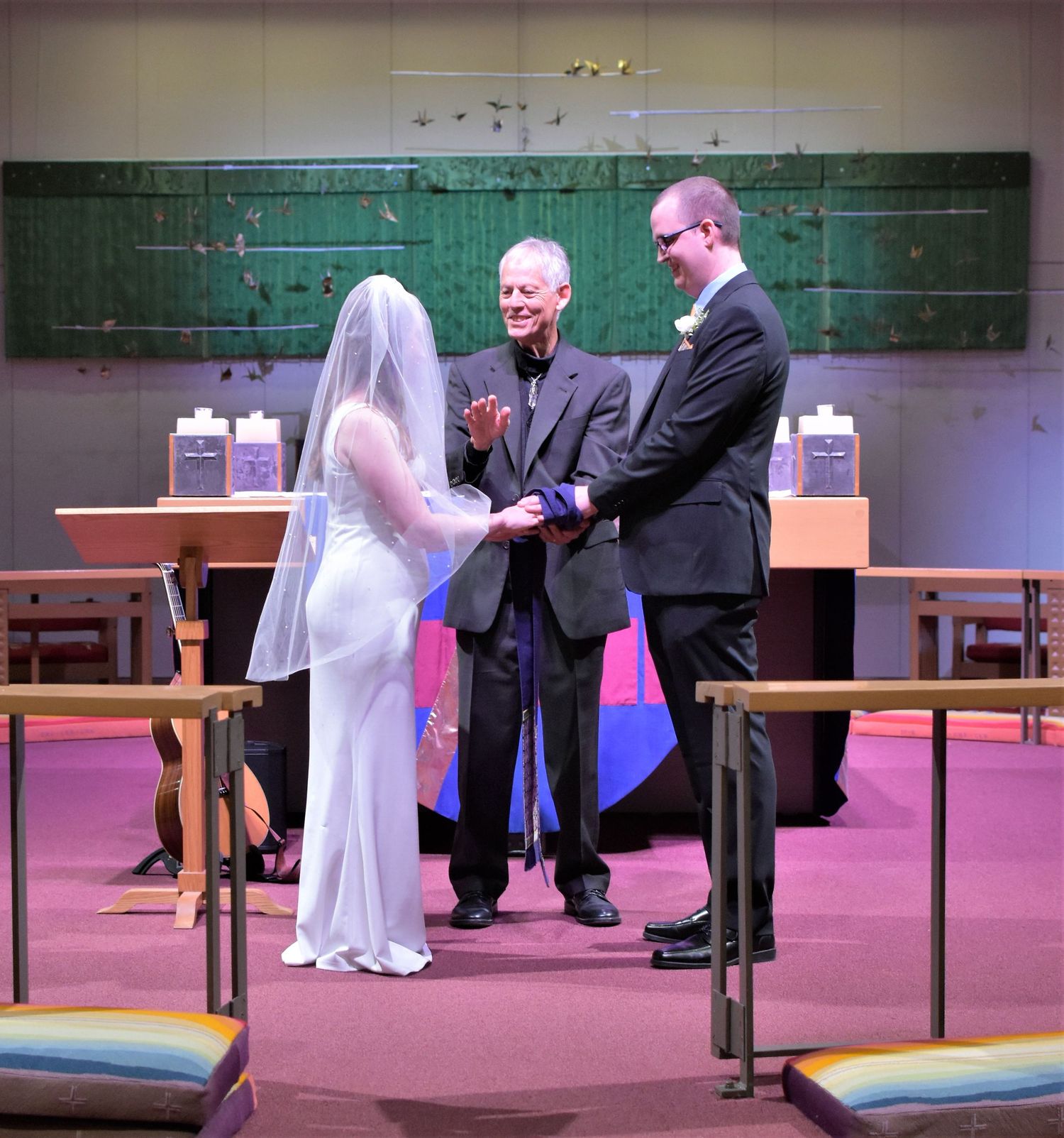 Bride and groom exchanging vows with officiant during indoor wedding ceremony at decorated altar.