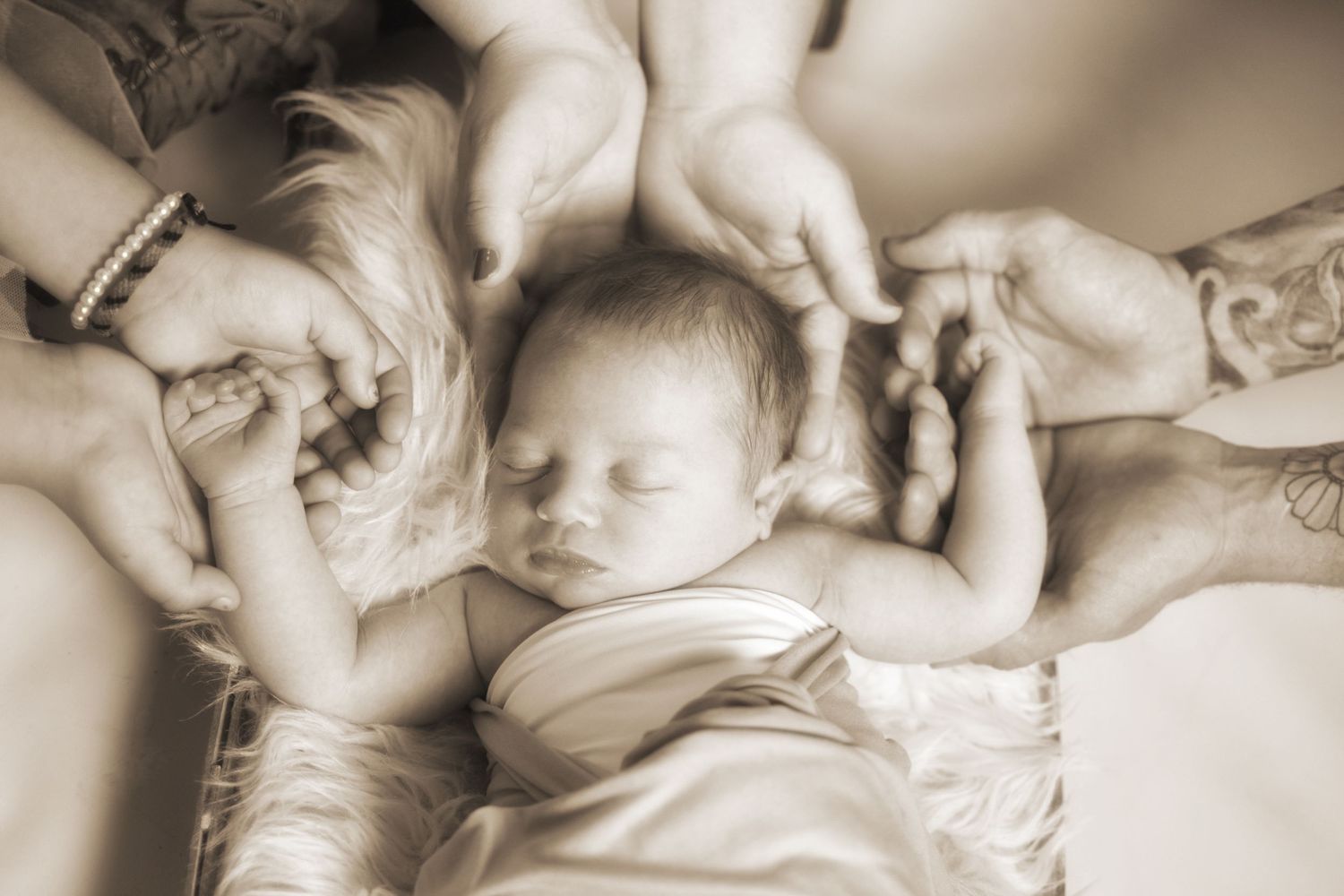 Artistic sepia portrait of sleeping newborn on textured background holding families' hands, San Antonio newborn photography