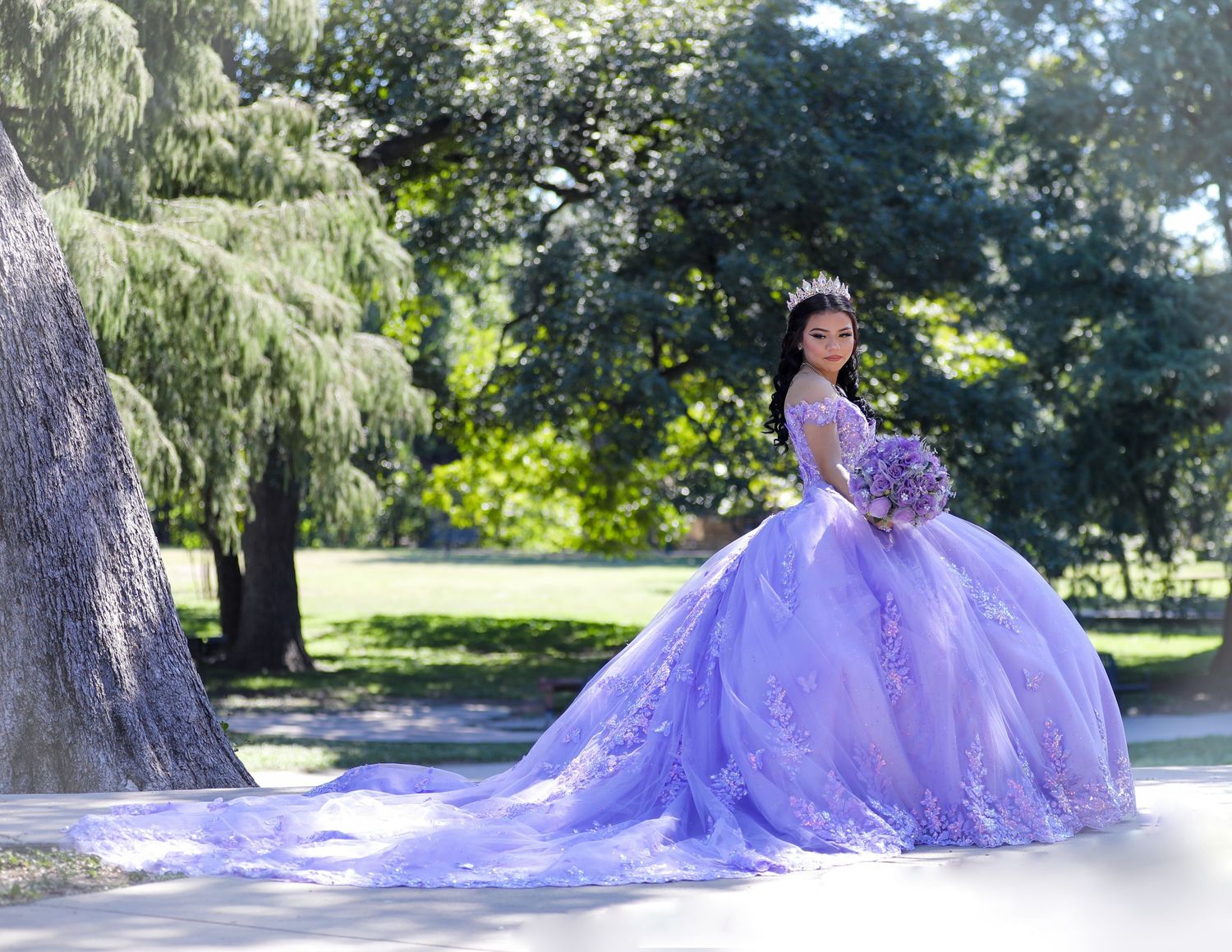 A flowing purple ballgown with a dramatic train photographed in a sunlit area at Riverwalk in San Antonio, quinceanera photography