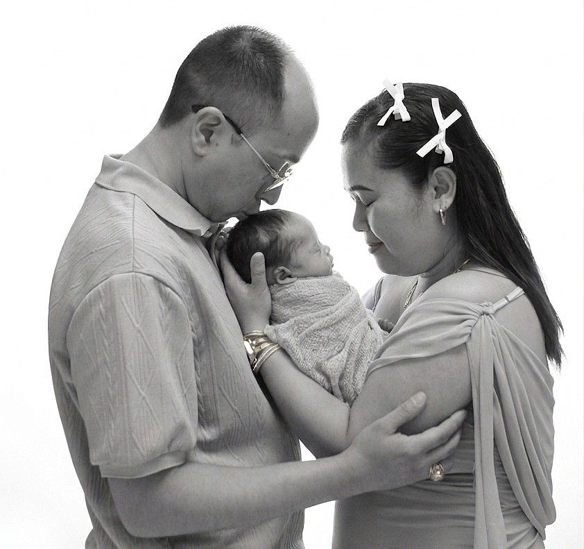 Black and white photo of parents lovingly cradling their newborn baby together in a studio setting.