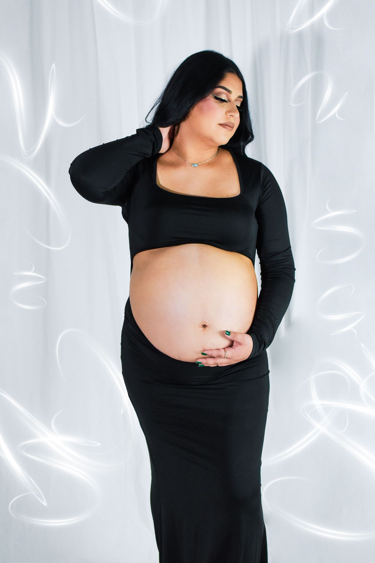 A maternity photoshoot showing a woman in a black dress with a peek a boo showing her baby bump in studio in San Antonio, Texas