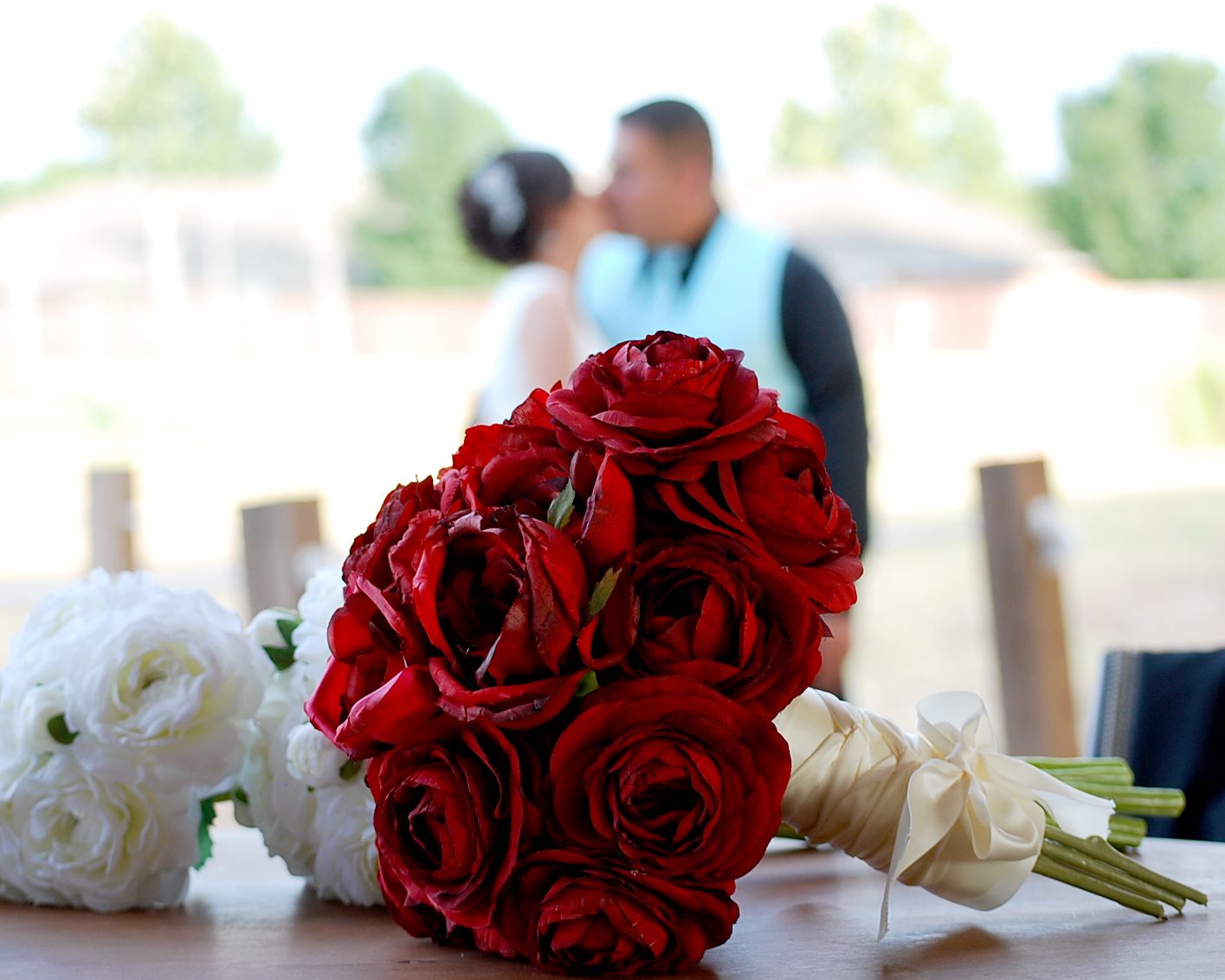 Red roses arranged in an elegant wedding bouquet with greenery accents and couple blurred in background, San Antonio wedding photography