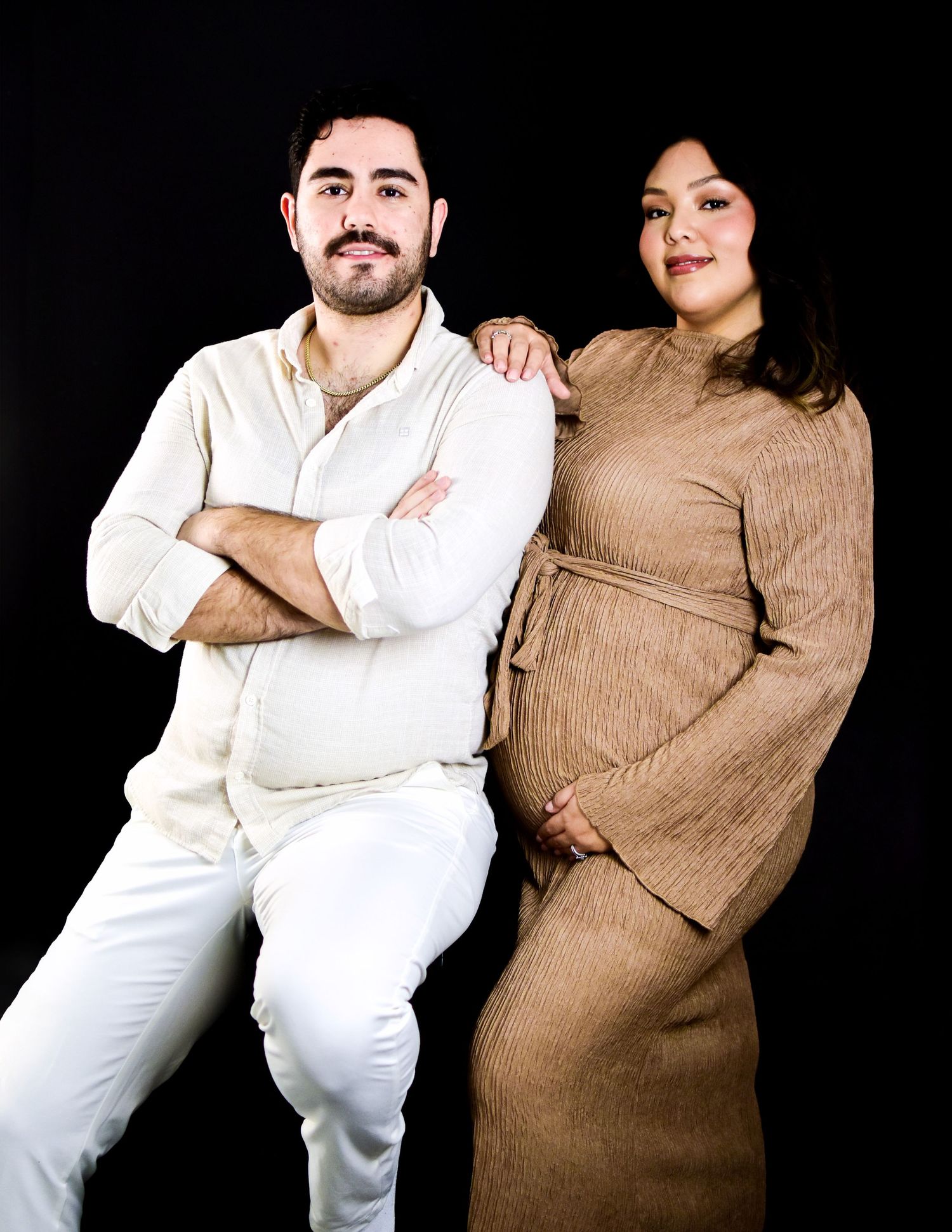 A couple poses together against a black background in a candid maternity photo in San Antonio, Texas Photographed by Precious Keepsakes.