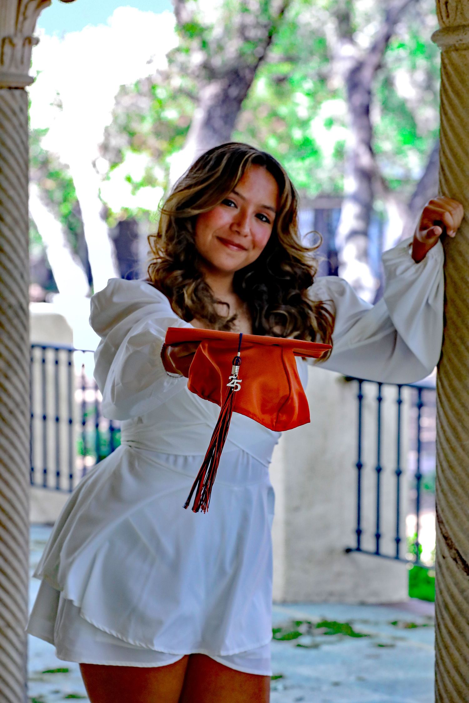 An excited student showing her graduation cap and tassel at her senior photography session at Landa Library in San Antonio, Texas.