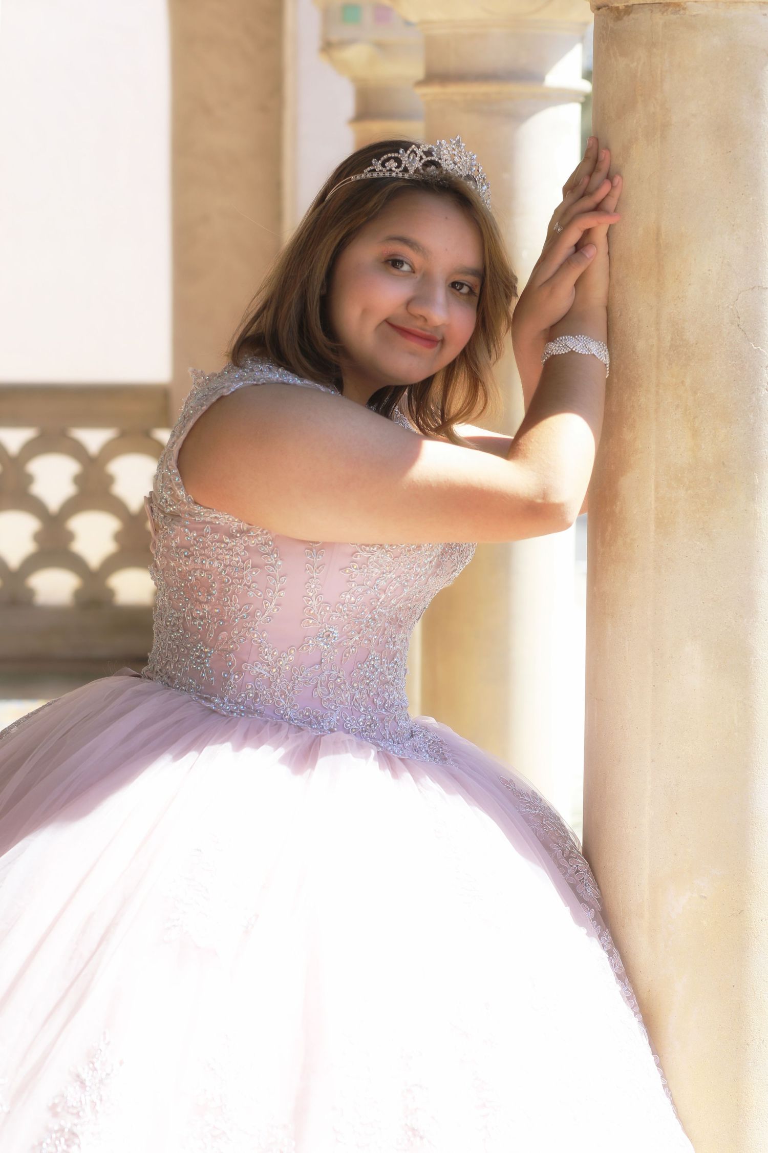 A princess in a pink ball gown and tiara poses elegantly at the McNay Museum during her quinceanera photography dress session.