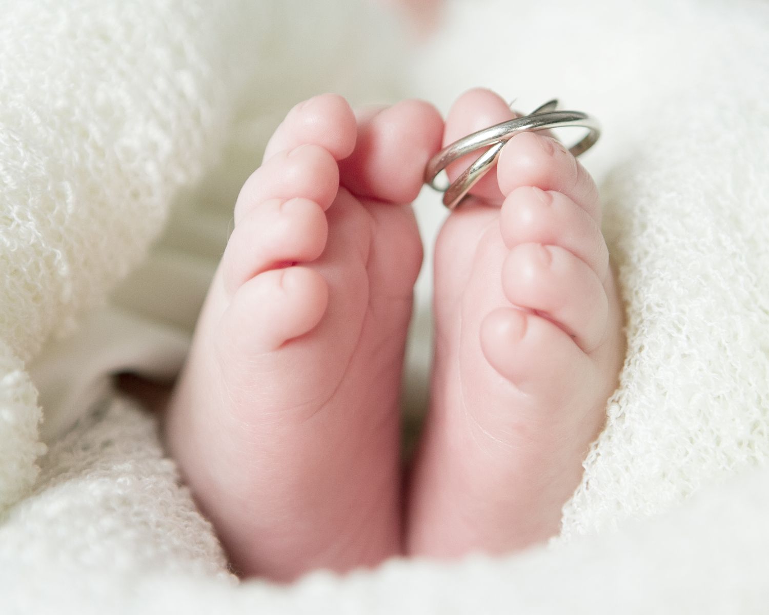 Close-up of tiny newborn toes wrapped in soft white blanket with parents wedding rings, San Antonio newborn photography