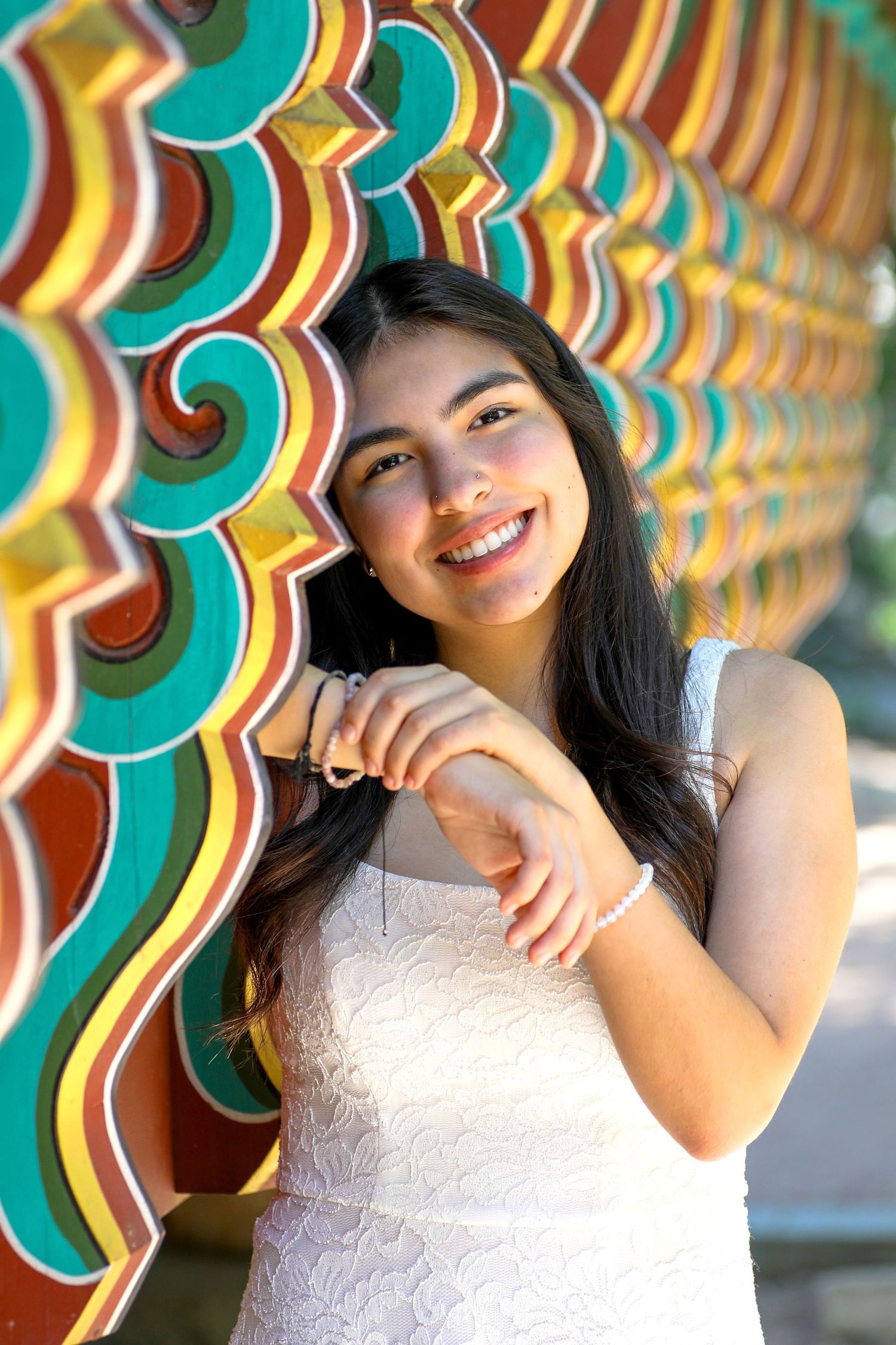Student against vibrant turquoise and orange decorative wall pattern showing joyful expression and white dress at her senior photo session