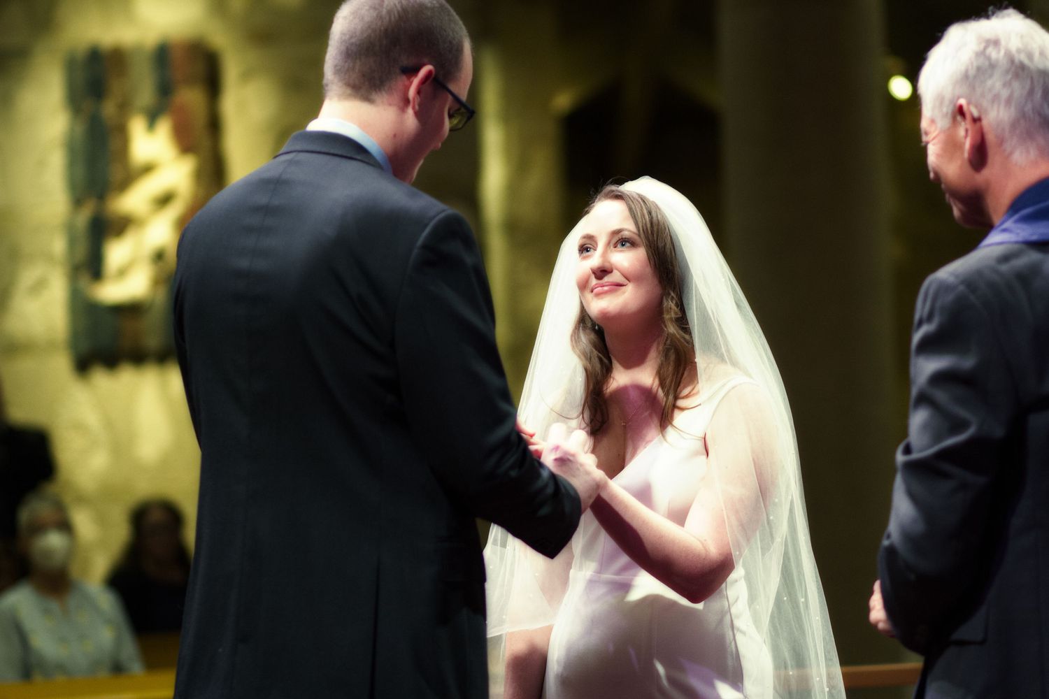 Bride and groom exchanging vows at a church wedding ceremony, bride wearing veil and gown.