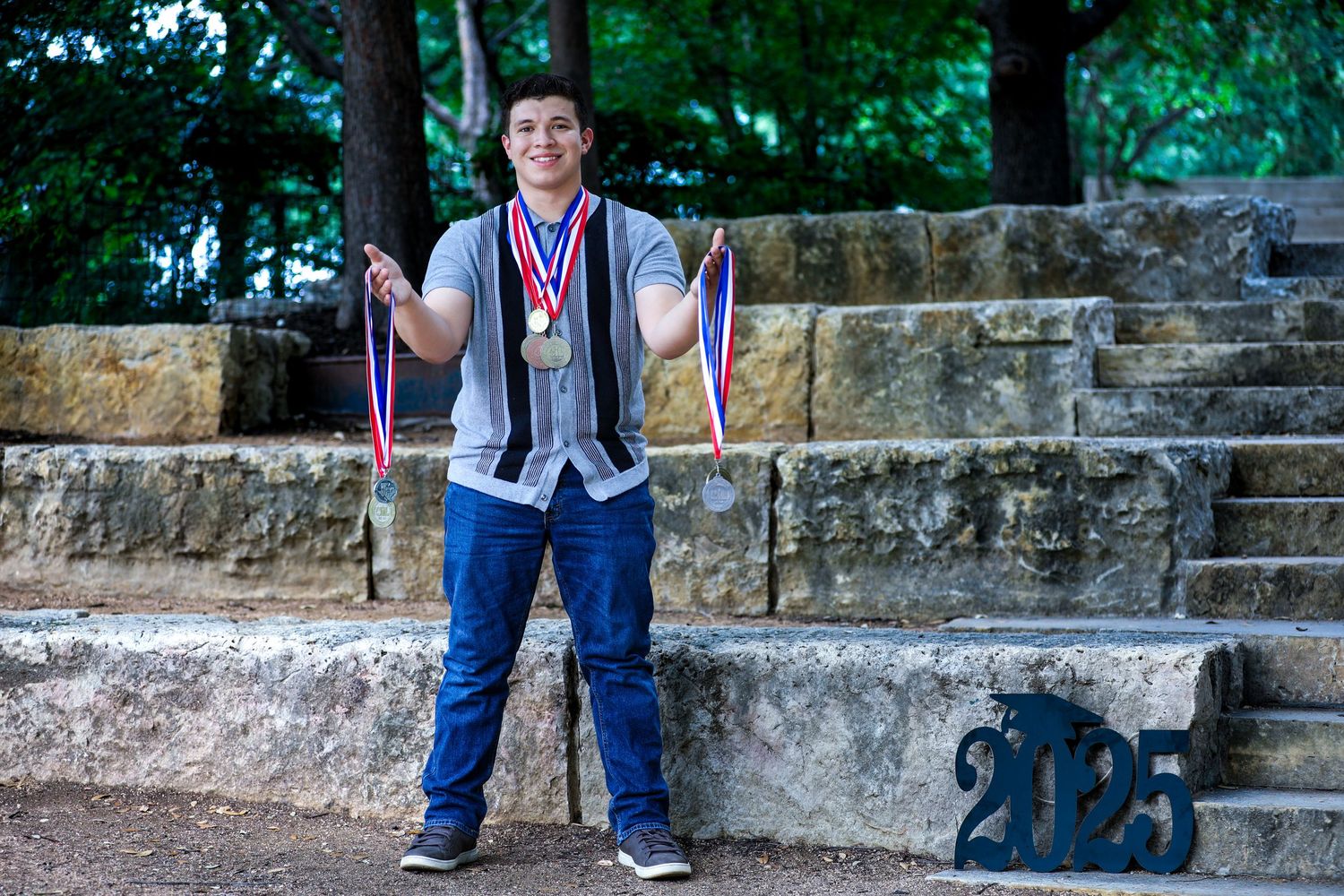 Student wearing blue jeans and sneakers stands on stone steps in at The Pearl for his senior photography session in San Antonio, Texas