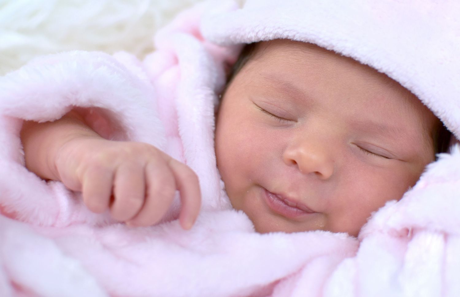 Peaceful newborn baby sleeping wrapped in soft pink blanket and hat with a gentle smile.