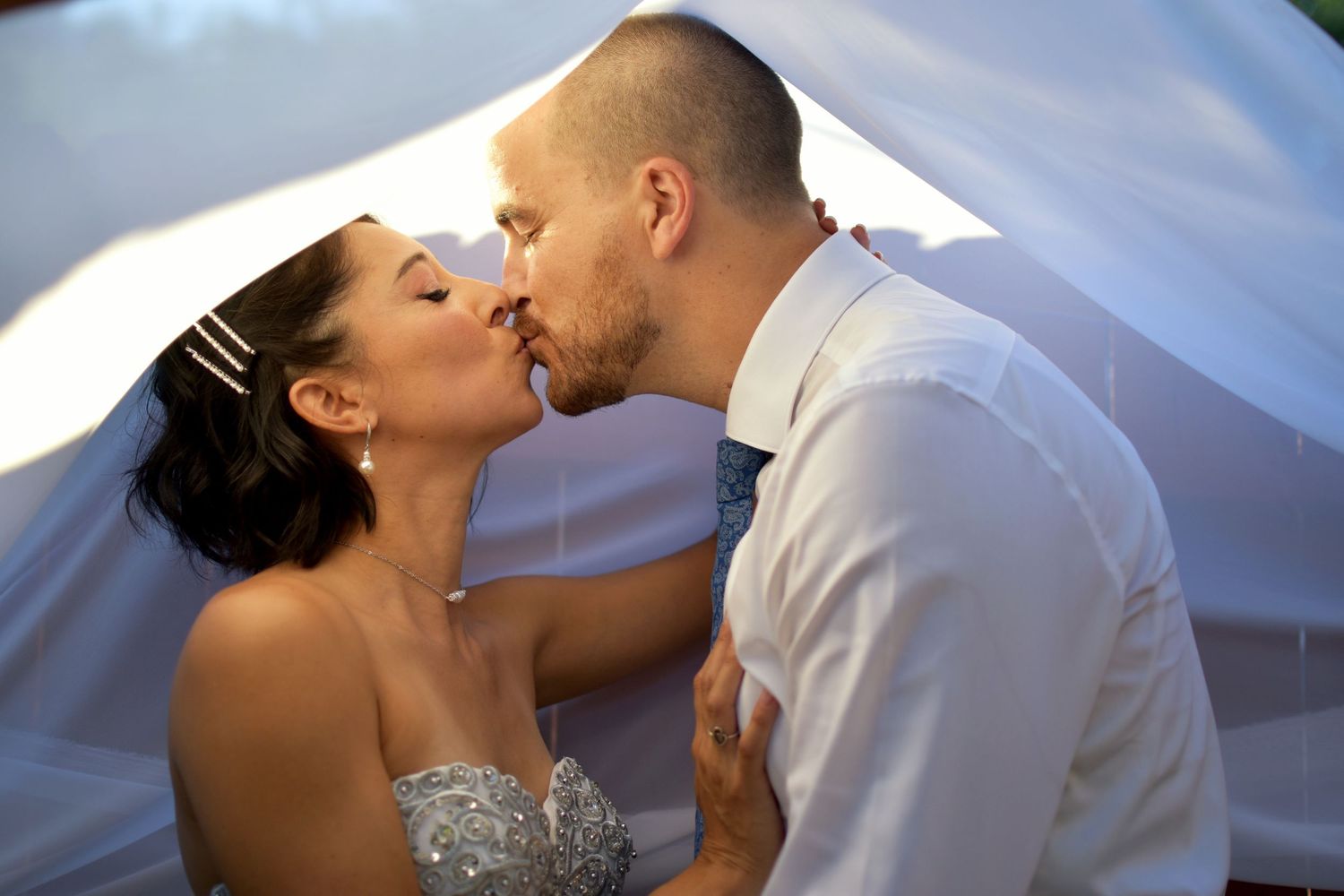 A Romantic backyard wedding couple sharing a tender kiss under a white veil during their special day in Boerne, Texas.