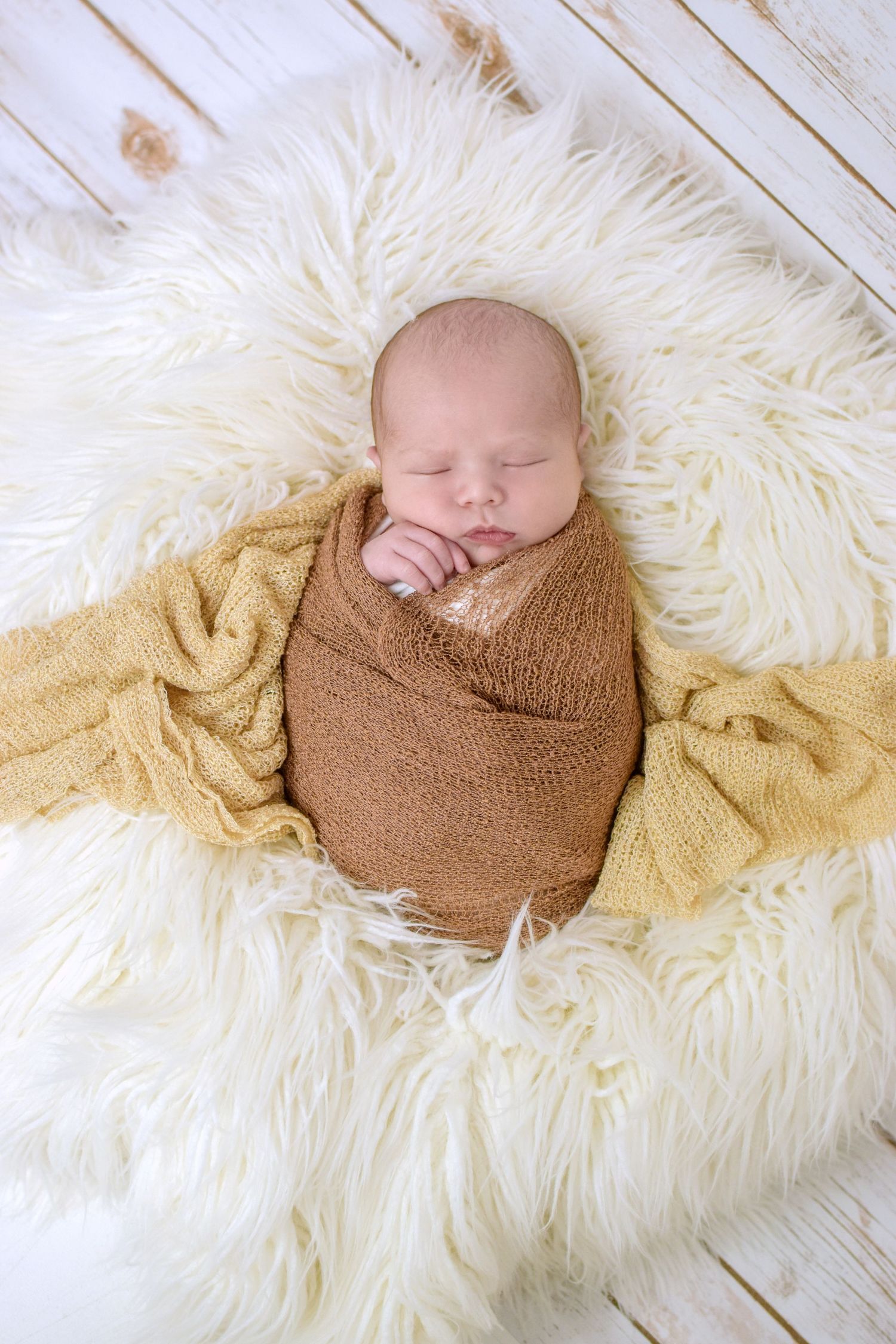Sleeping newborn wrapped in brown knit on cream fur rug. San Antonio newborn photography