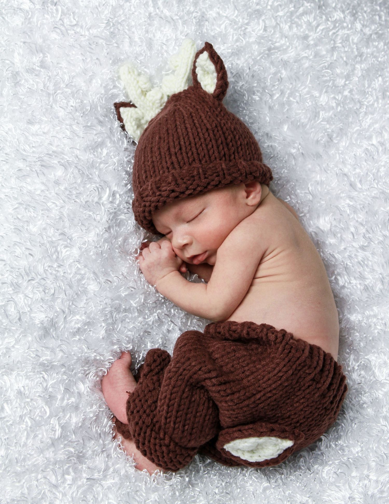 Baby wearing brown knit deer outfit sleeping on white textured surface, San Antonio newborn photography session during holidays