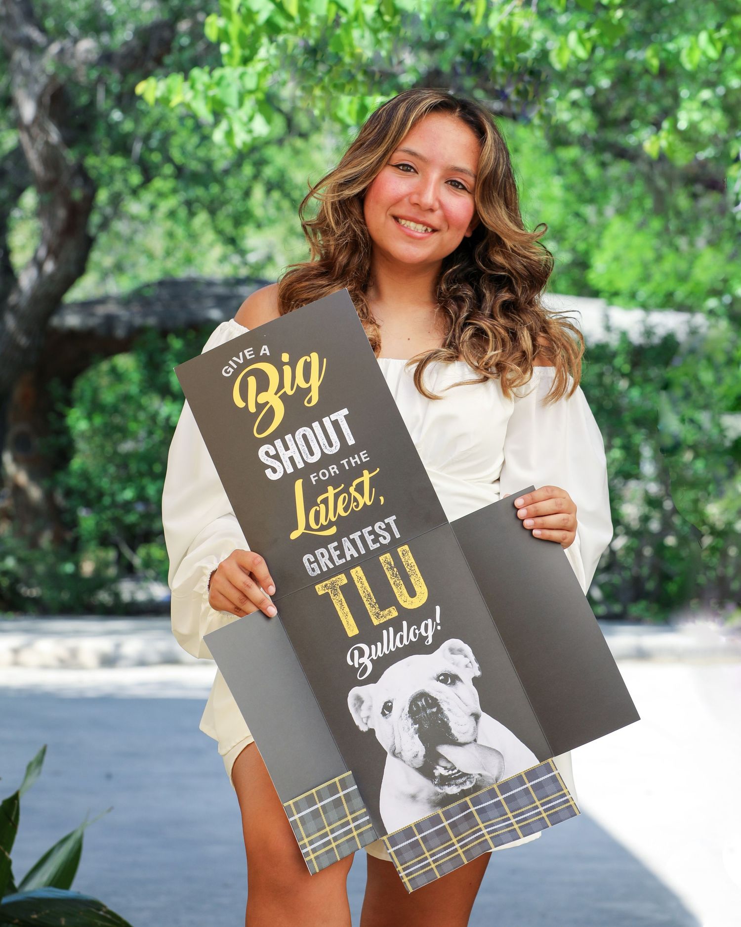 A student holding up her TLU acceptance sign with bulldog-themed text at her senior photo session at Landa Library in San Antonio, Texas