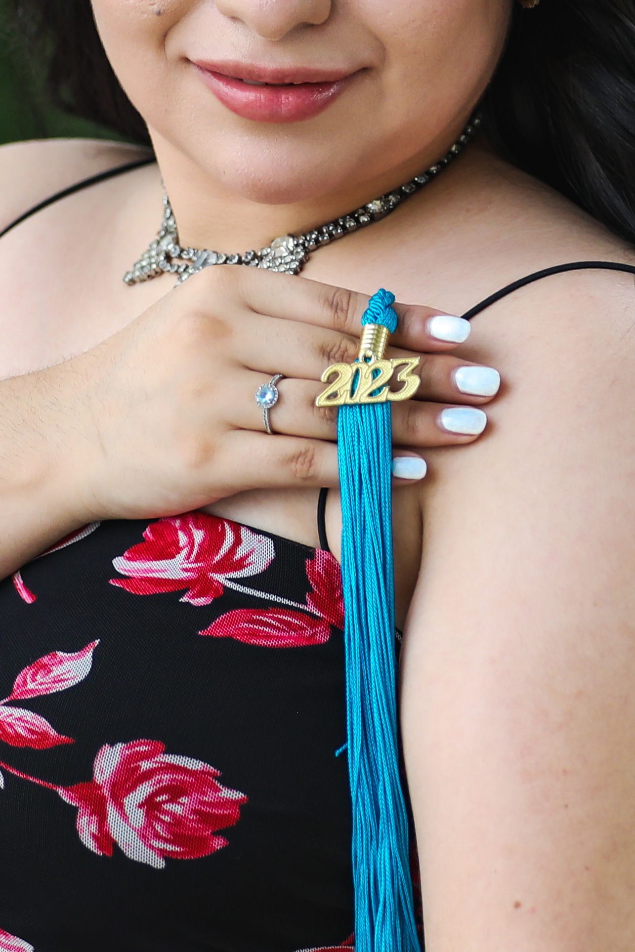 A student showing her turquoise tassel with white nail polish and floral print clothing at her LSU graduation photo session at Conception Pk
