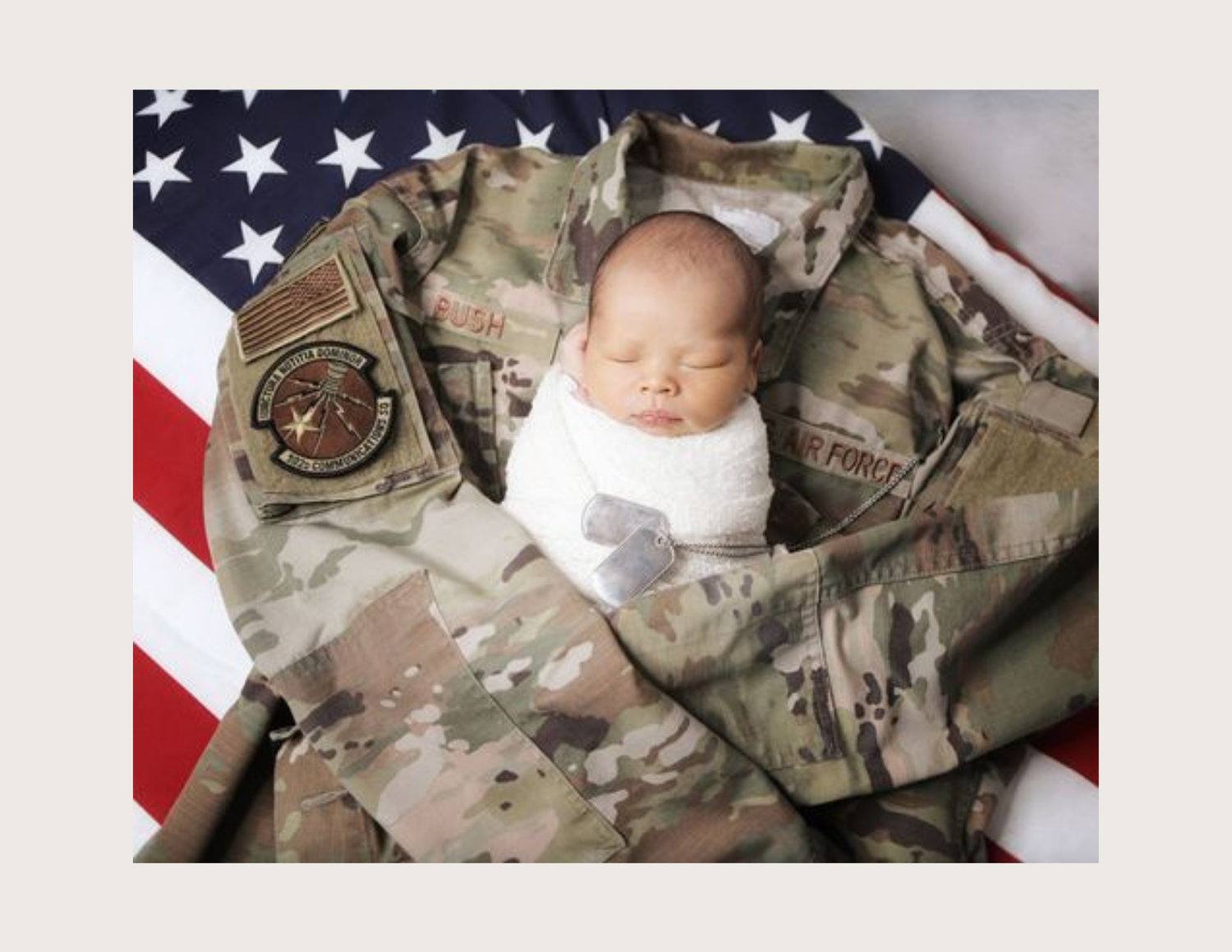 Newborn baby swaddled in white sleeping on a U.S. Air Force camouflage uniform with an American flag backdrop.