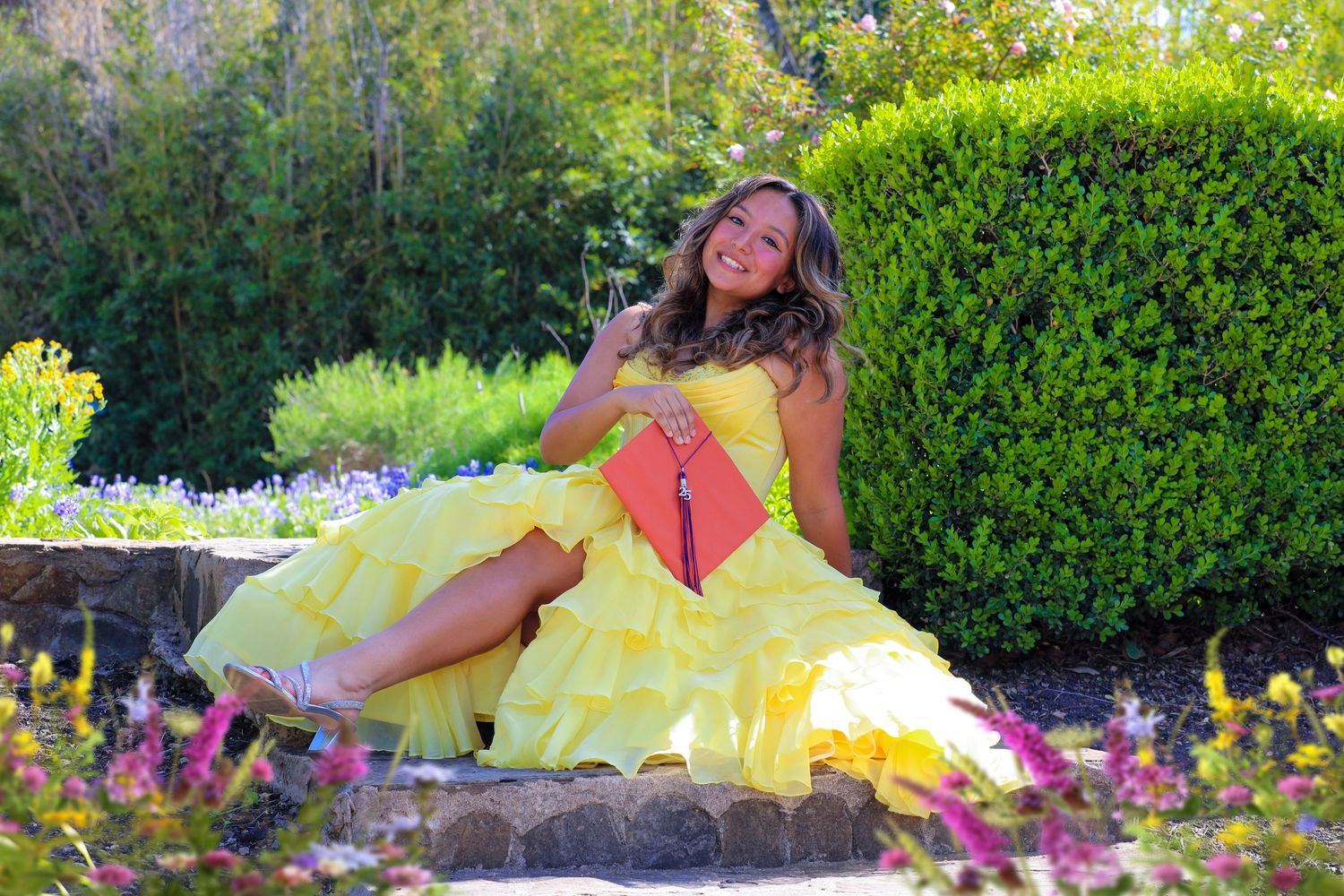 Student relaxes in a lush garden setting at Landa Library with yellow flowers at her senior photography session.